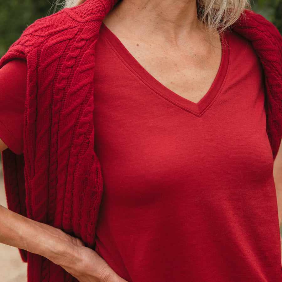 A close-up of a woman wearing a red short-sleeve V-neck t-shirt with a matching red cable-knit draped over her shoulders.