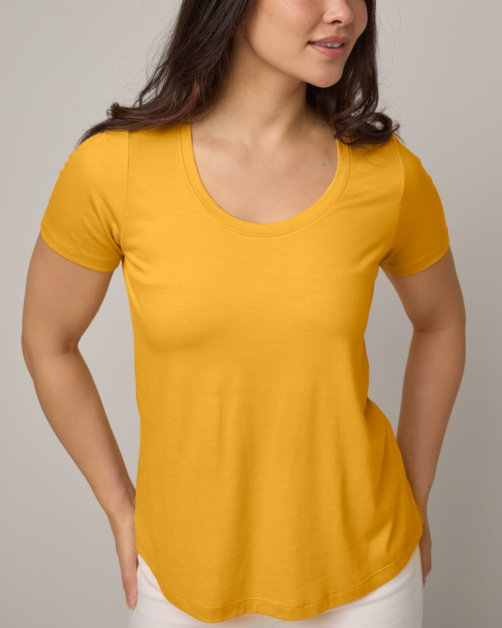Model wearing Stella Scoop Neck Tee in Mango, a warm sunshine yellow color. Stella Scoop Neck Tee is a merino wool short sleeve, scoop neck t-shirt available in sizes XS-3X.