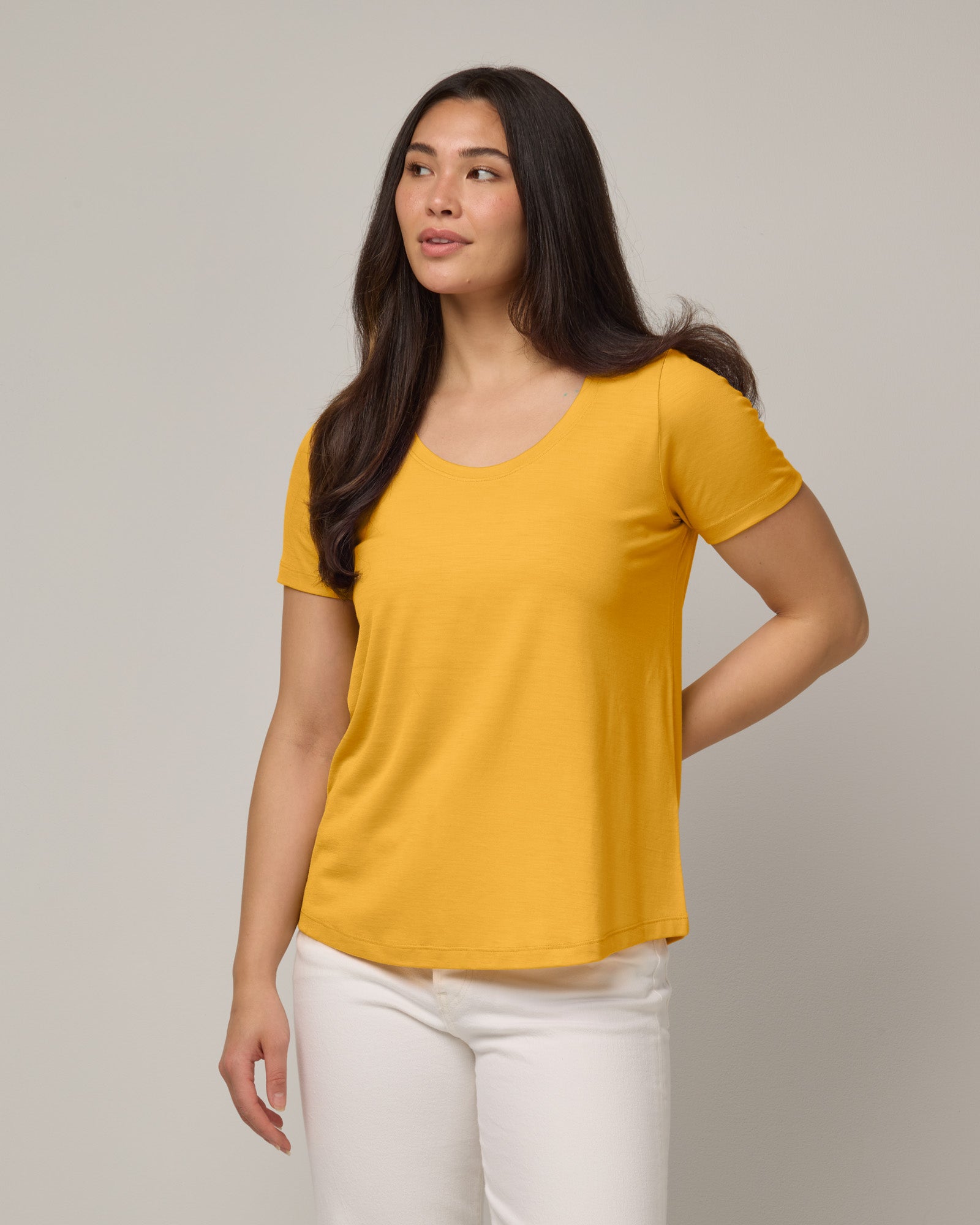 Model wearing Stella Scoop Neck Tee in Mango, a warm sunshine yellow color. Stella Scoop Neck Tee is a merino wool short sleeve, scoop neck t-shirt available in sizes XS-3X.