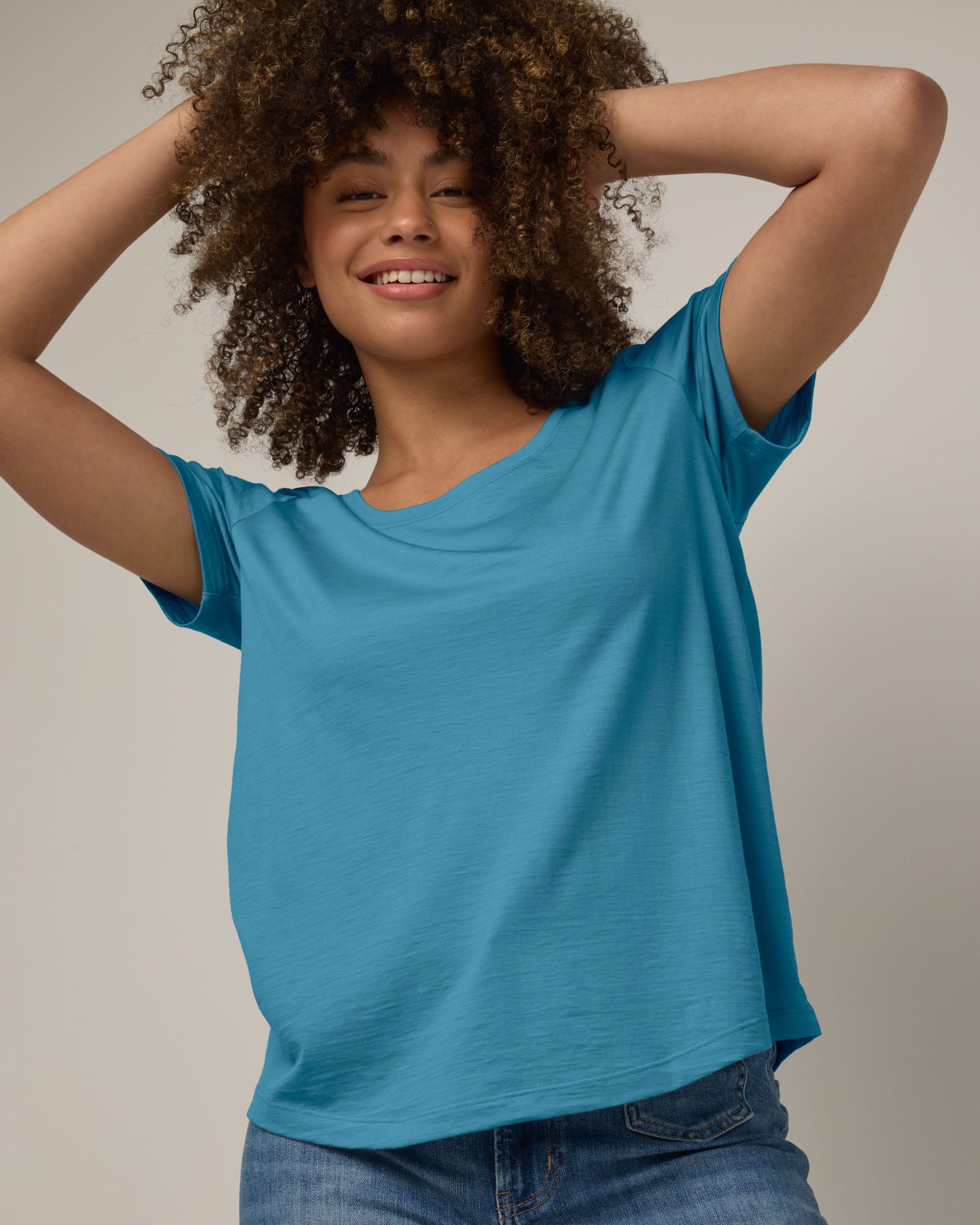 Model wearing Stella Scoop Neck Tee in Alpine Blue, a glacier ice blue color. Stella Scoop Neck Tee is a merino wool short sleeve, scoop neck t-shirt available in sizes XS-3X.