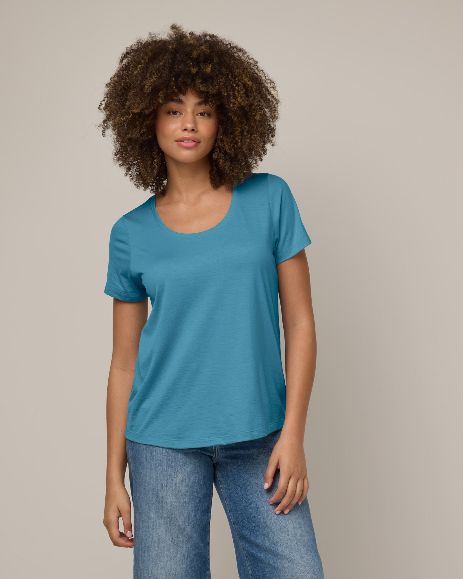 Model wearing Stella Scoop Neck Tee in Alpine Blue, a glacier ice blue color. Stella Scoop Neck Tee is a merino wool short sleeve, scoop neck t-shirt available in sizes XS-3X.