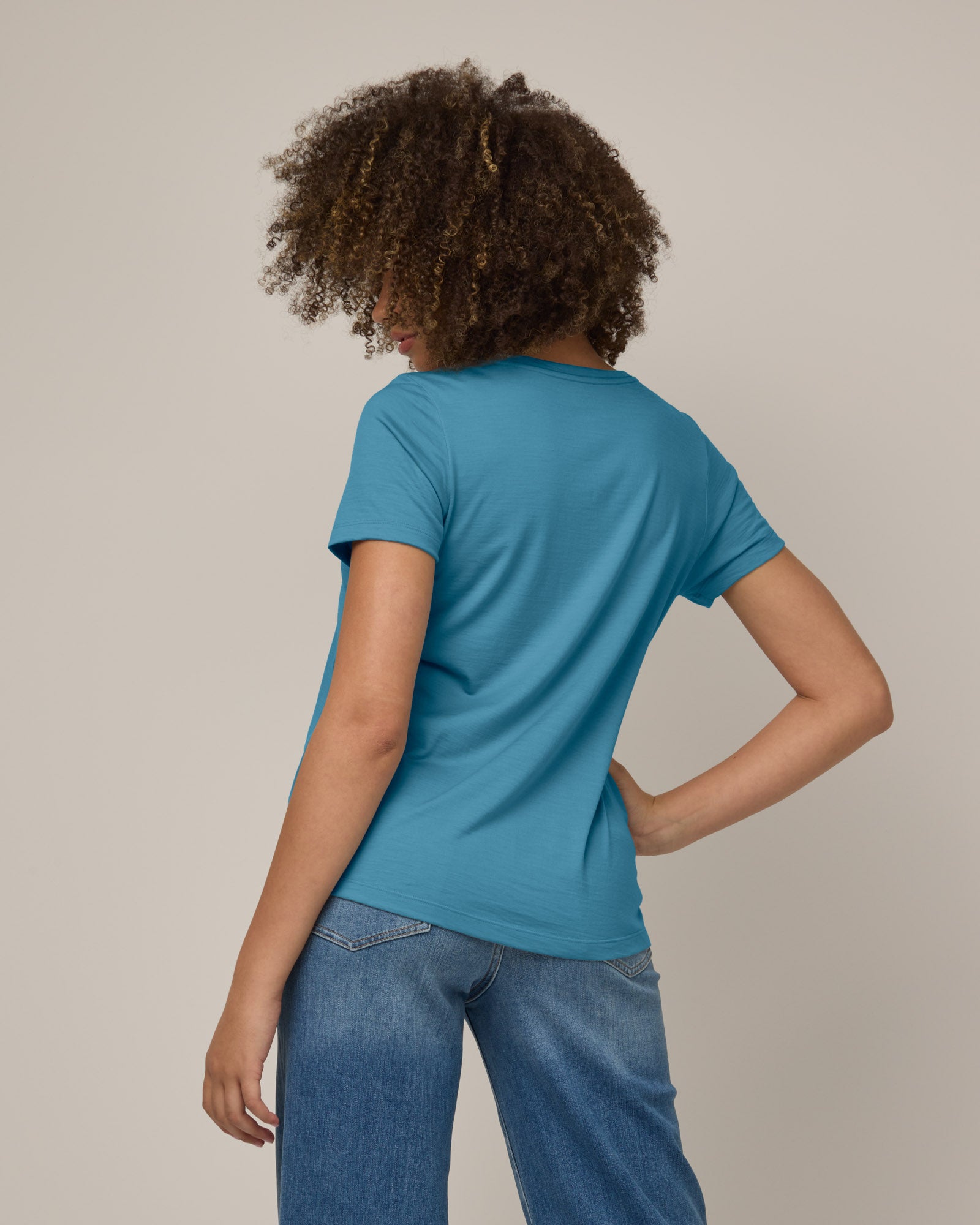 Model wearing Stella Scoop Neck Tee in Alpine Blue, a glacier ice blue color. Stella Scoop Neck Tee is a merino wool short sleeve, scoop neck t-shirt available in sizes XS-3X.