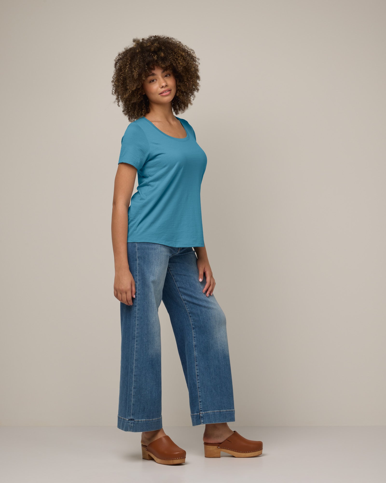Model wearing Stella Scoop Neck Tee in Alpine Blue, a glacier ice blue color. Stella Scoop Neck Tee is a merino wool short sleeve, scoop neck t-shirt available in sizes XS-3X.