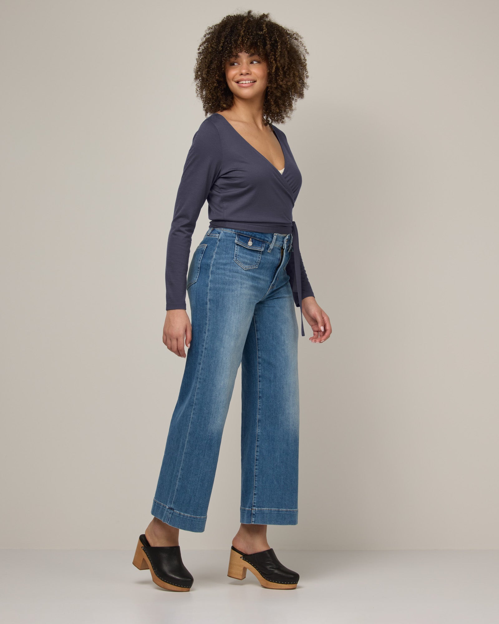 Model wearing Natalia Wrap Top in Odyssey Gray, a slate blue-gray color. Natalia Wrap Top is a merino wool long sleeve, v-neck, slim fit top available in sizes XS-3X.