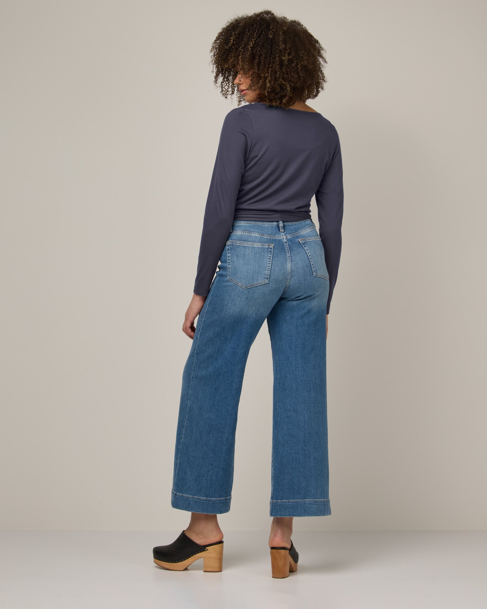 Model wearing Natalia Wrap Top in Odyssey Gray, a slate blue-gray color. Natalia Wrap Top is a merino wool long sleeve, v-neck, slim fit top available in sizes XS-3X.