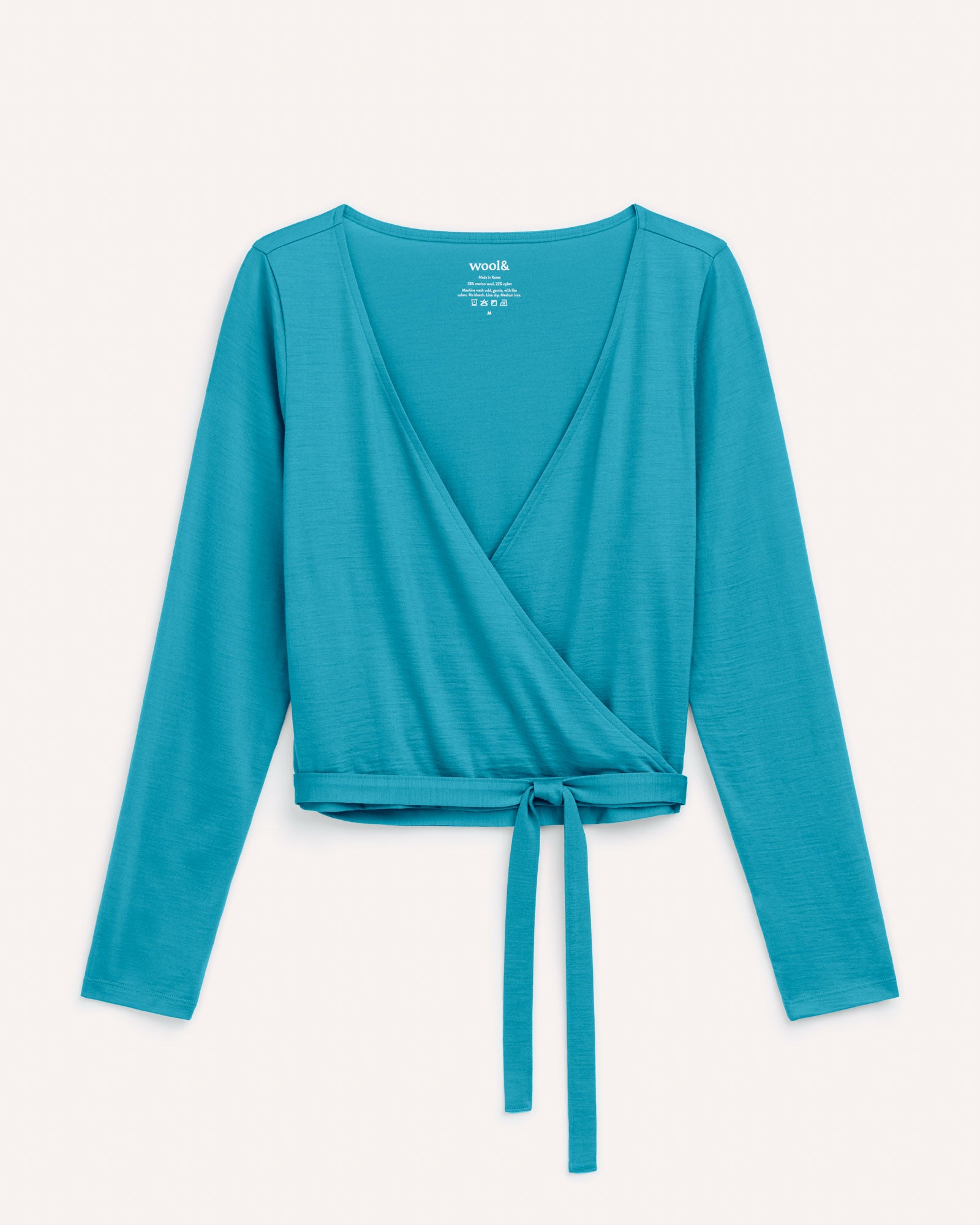 Laydown of Natalia Wrap Top in Sea Blue, a bright sky blue color. Natalia Wrap Top is a merino wool long sleeve, v-neck, slim fit top available in sizes XS-3X.