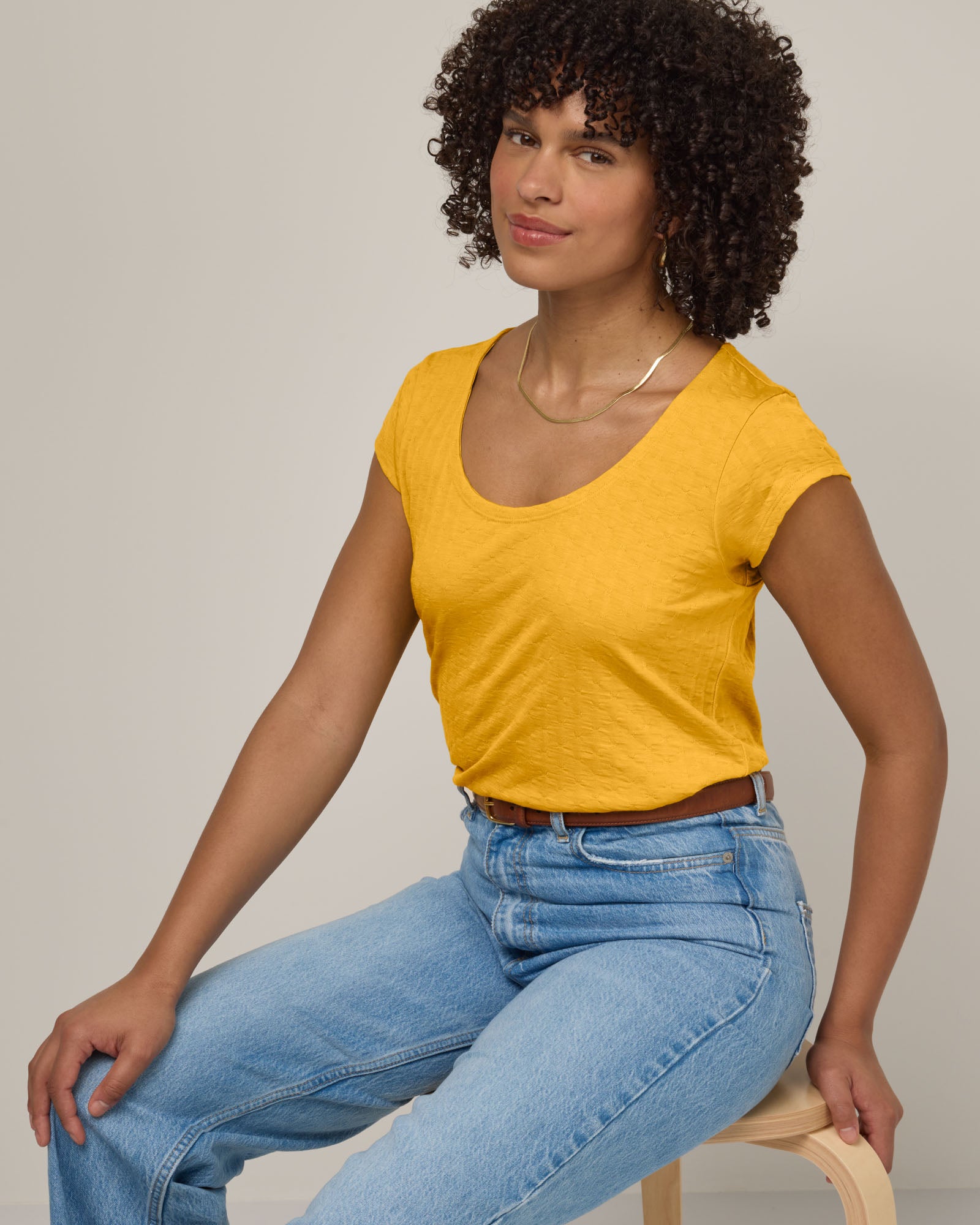 Model wearing Savanna Cap Sleeve Tee in Mango, a warm sunshine yellow color. Savanna Cap Sleeve Tee is a merino wool short sleeve, scoop neck, regular fit tee available in sizes XS-XXL.