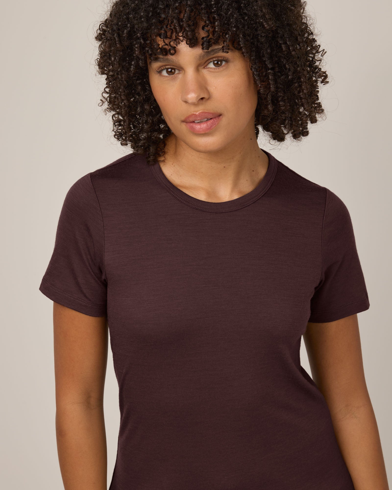 Model wearing Cara 100% Wool Fitted Tee in Espresso, a warm deep brown color. Cara 100% Wool Fitted Tee is a merino wool short sleeve, crew neck, slim fit tee available in sizes XS-3X.