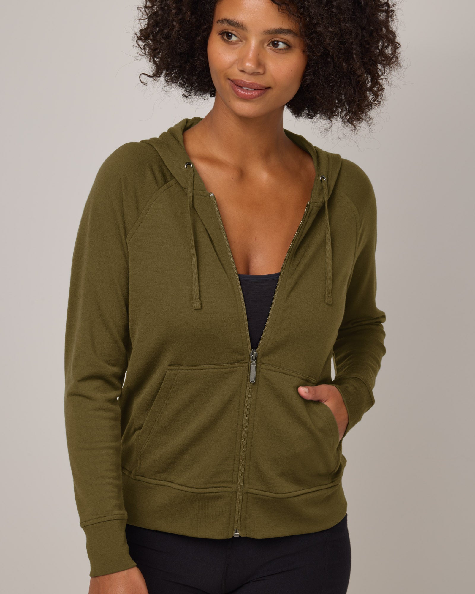Model wearing Aspen Full-Zip Hoodie in Olive. Aspen Full-Zip Hoodie is a merino wool long sleeve zip hoodie with pockets available in sizes XS-3X.