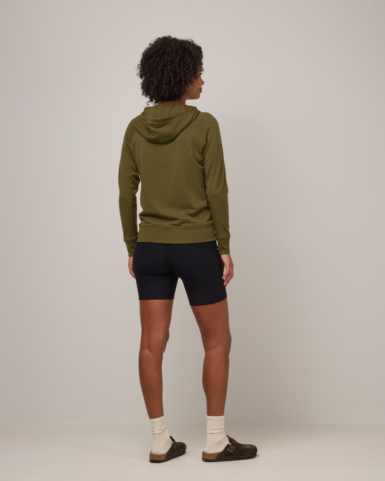 Model wearing Aspen Full-Zip Hoodie in Olive. Aspen Full-Zip Hoodie is a merino wool long sleeve zip hoodie with pockets available in sizes XS-3X.