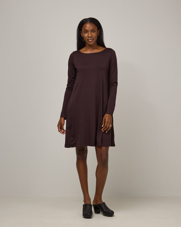 Model wearing Rowena Swing Dress in Espresso, a dark brown color. Rowena Swing Dress is a merino wool long sleeve, boatneck, knee length swing dress with pockets available in sizes XS-3X Regular, XS-3X Long.