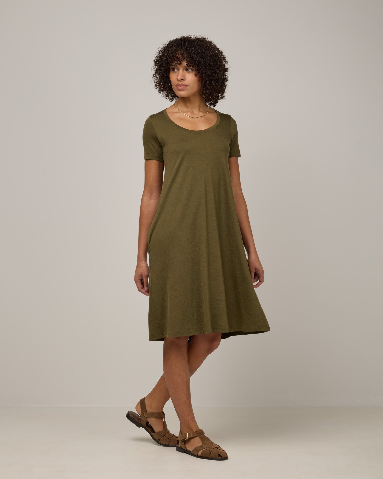 Model wearing Maggie Swing Dress in Olive. Maggie Swing Dress is a merino wool short sleeve, scoop neck, knee length swing dress with pockets available in sizes XS-3X Regular, XS-3X Long.