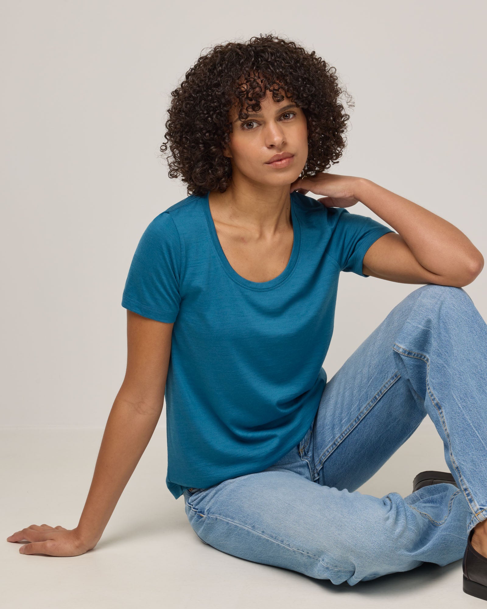 Model wearing Stella Signature Scoop Neck Tee in Ocean Teal, a medium blue-green color. Stella Signature Scoop Neck Tee is a merino wool short sleeve, scoop neck, relaxed fit tee available in sizes XS-3X.