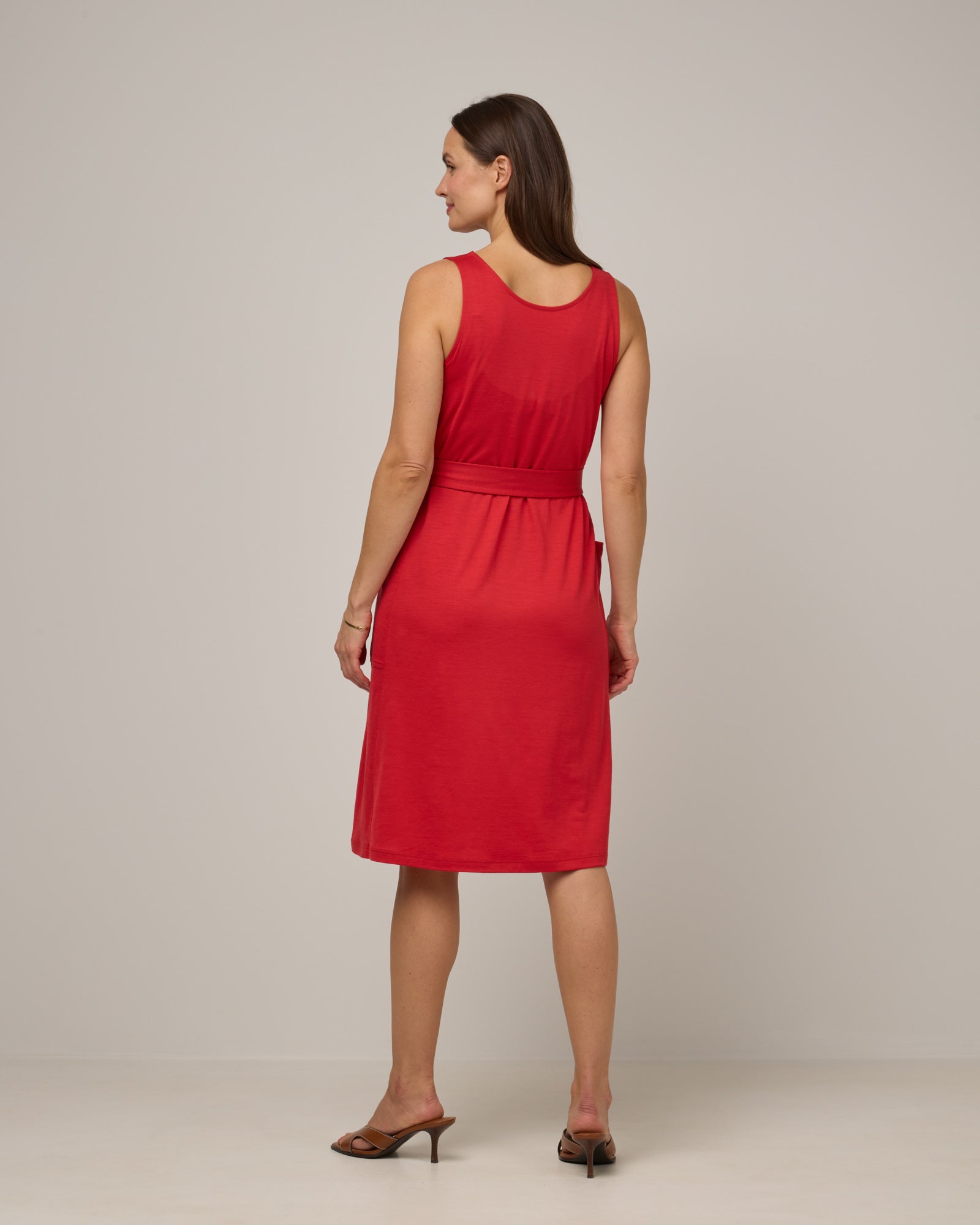 Model wearing Summer Reversible Dress in Fruit Punch, a vivid red-orange color. Summer Reversible Dress is a merino wool sleeveless, reversible, midi swing dress with pockets available in sizes XS-3X.