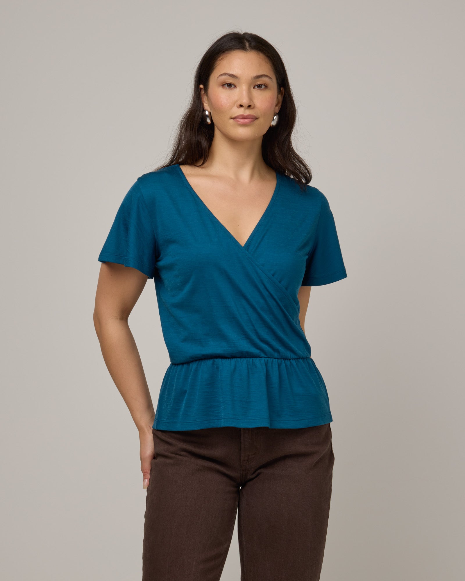 Model wearing Jeanne Flutter Sleeve Top in Ocean Teal, a medium blue-green color. Jeanne Flutter Sleeve Top is a merino wool short sleeve, reversible, regular fit top available in sizes XS-XXL.