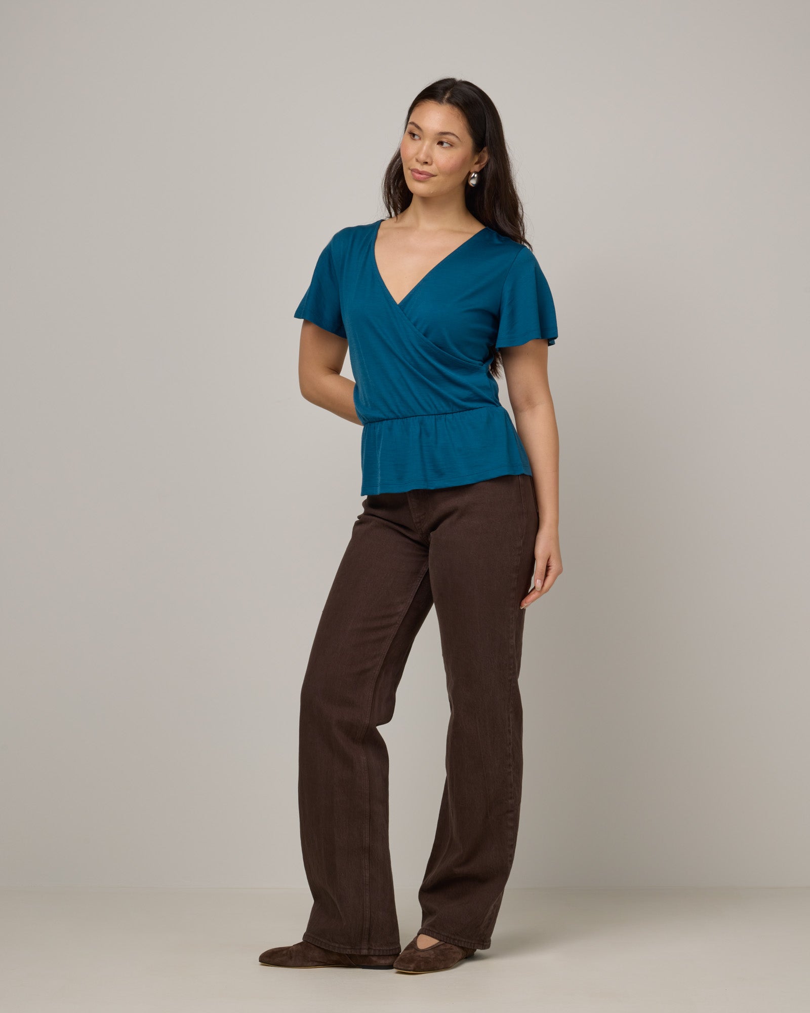 Model wearing Jeanne Flutter Sleeve Top in Ocean Teal, a medium blue-green color. Jeanne Flutter Sleeve Top is a merino wool short sleeve, reversible, regular fit top available in sizes XS-XXL.