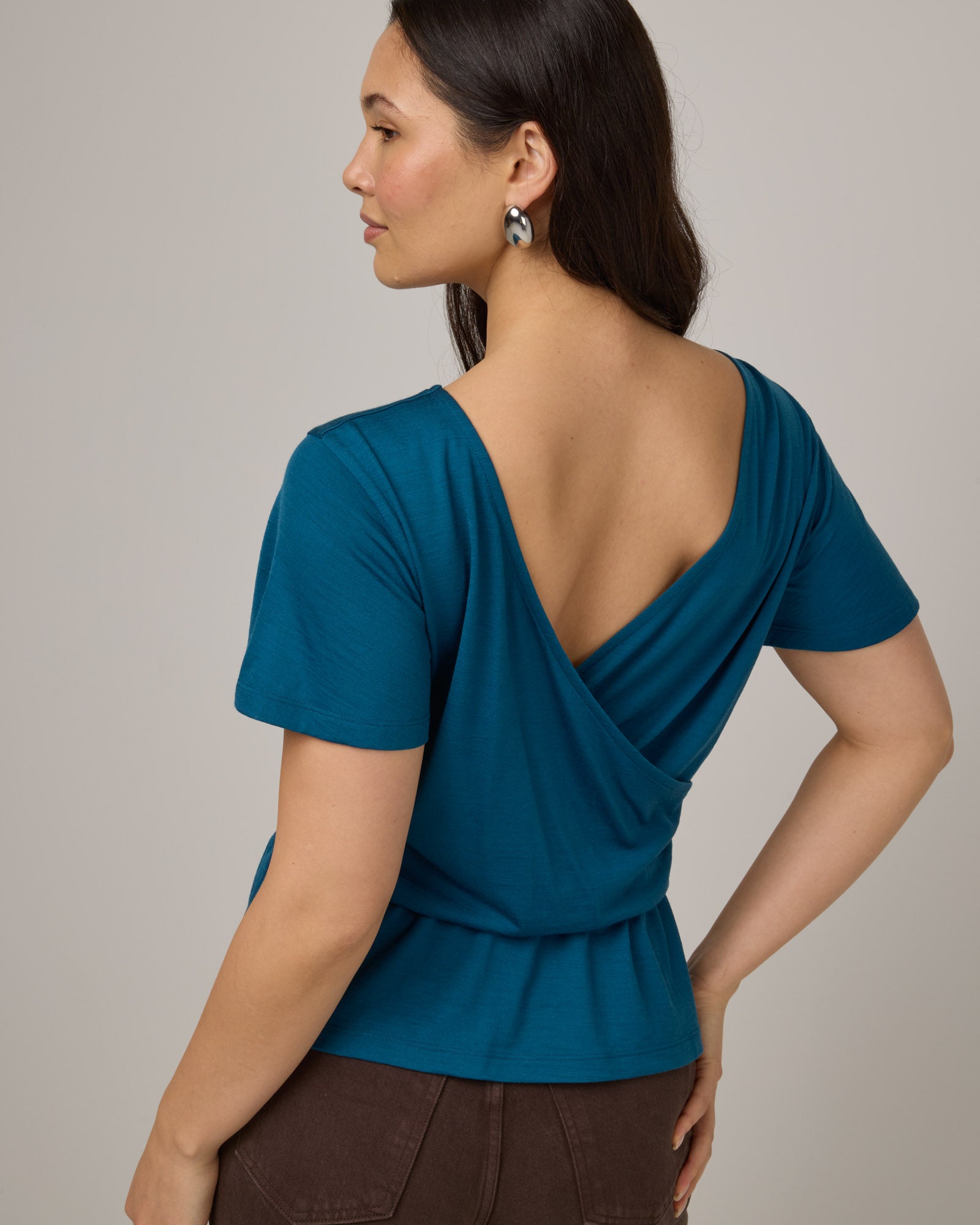 Model wearing Jeanne Flutter Sleeve Top in Ocean Teal, a medium blue-green color. Jeanne Flutter Sleeve Top is a merino wool short sleeve, reversible, regular fit top available in sizes XS-XXL.