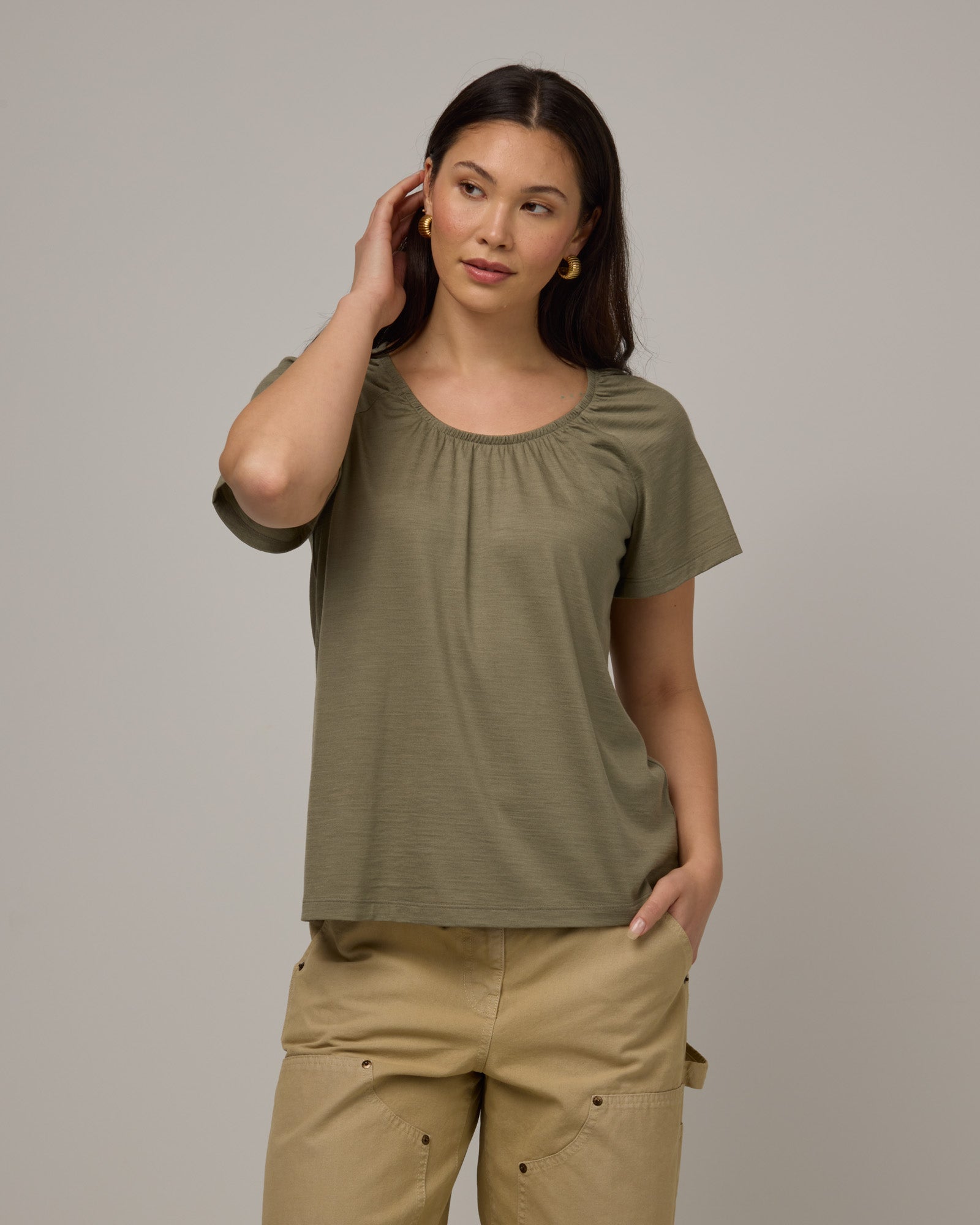 Model wearing Lilah Signature Gathered Neck Tee in Sage Green, a soft muted green color. Lilah Signature Gathered Neck Tee is a merino wool short sleeve, scoop neck, relaxed fit tee available in sizes XS-3X.