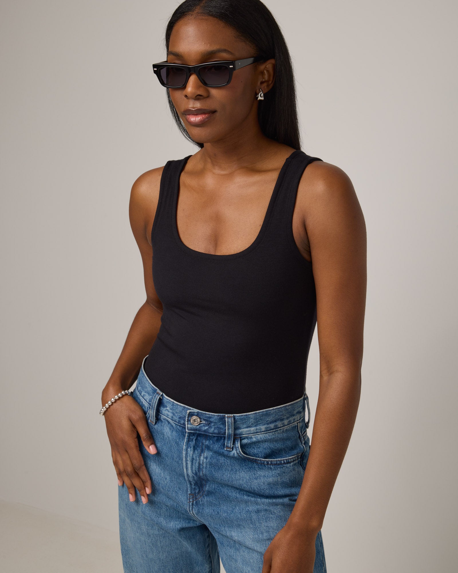Model wearing Britt Bodysuit in Black. Britt Bodysuit is a merino wool slim fit, sleeveless, scoop neck bodysuit available in sizes XS-XXL.