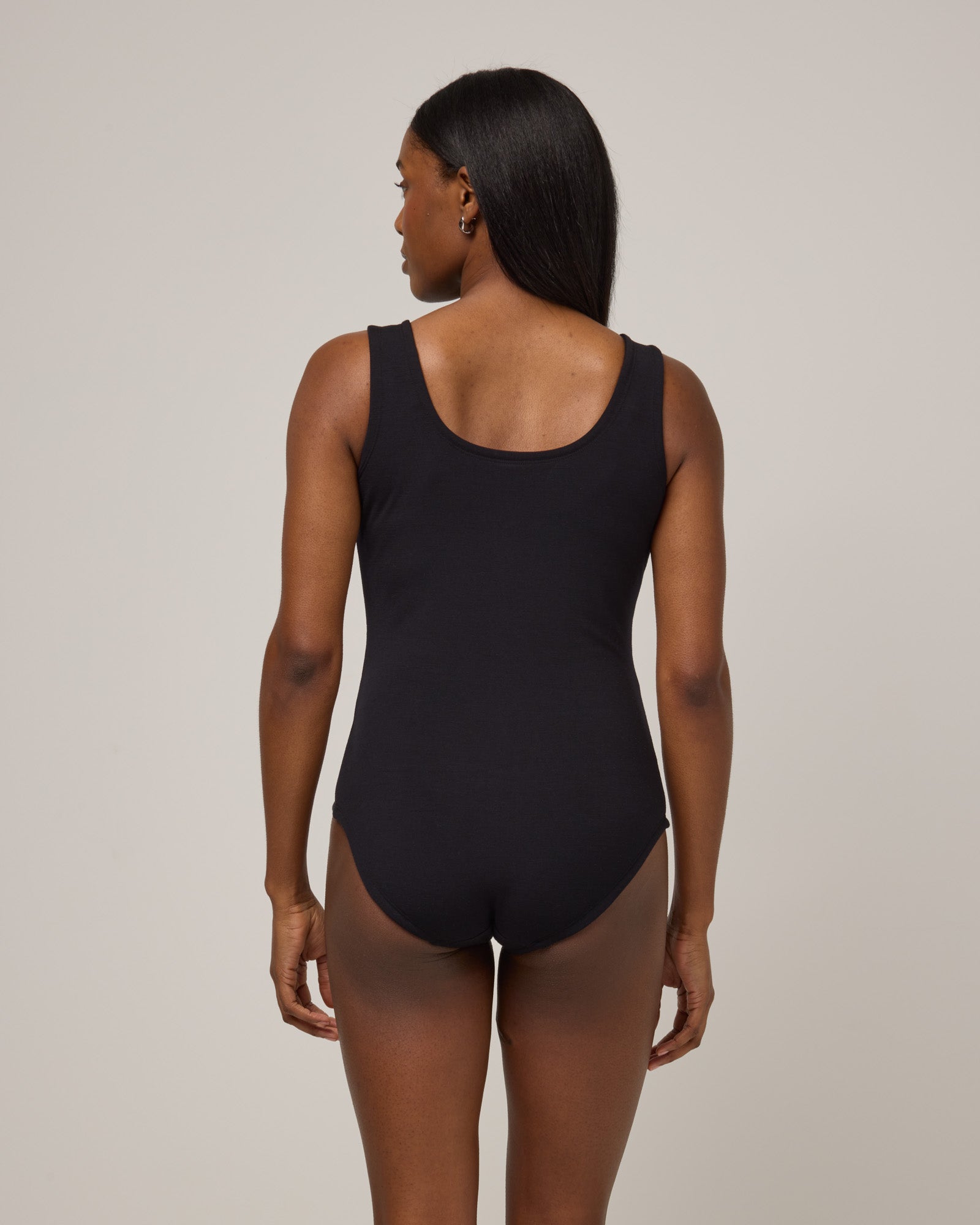 Model wearing Britt Bodysuit in Black. Britt Bodysuit is a merino wool slim fit, sleeveless, scoop neck bodysuit available in sizes XS-XXL.