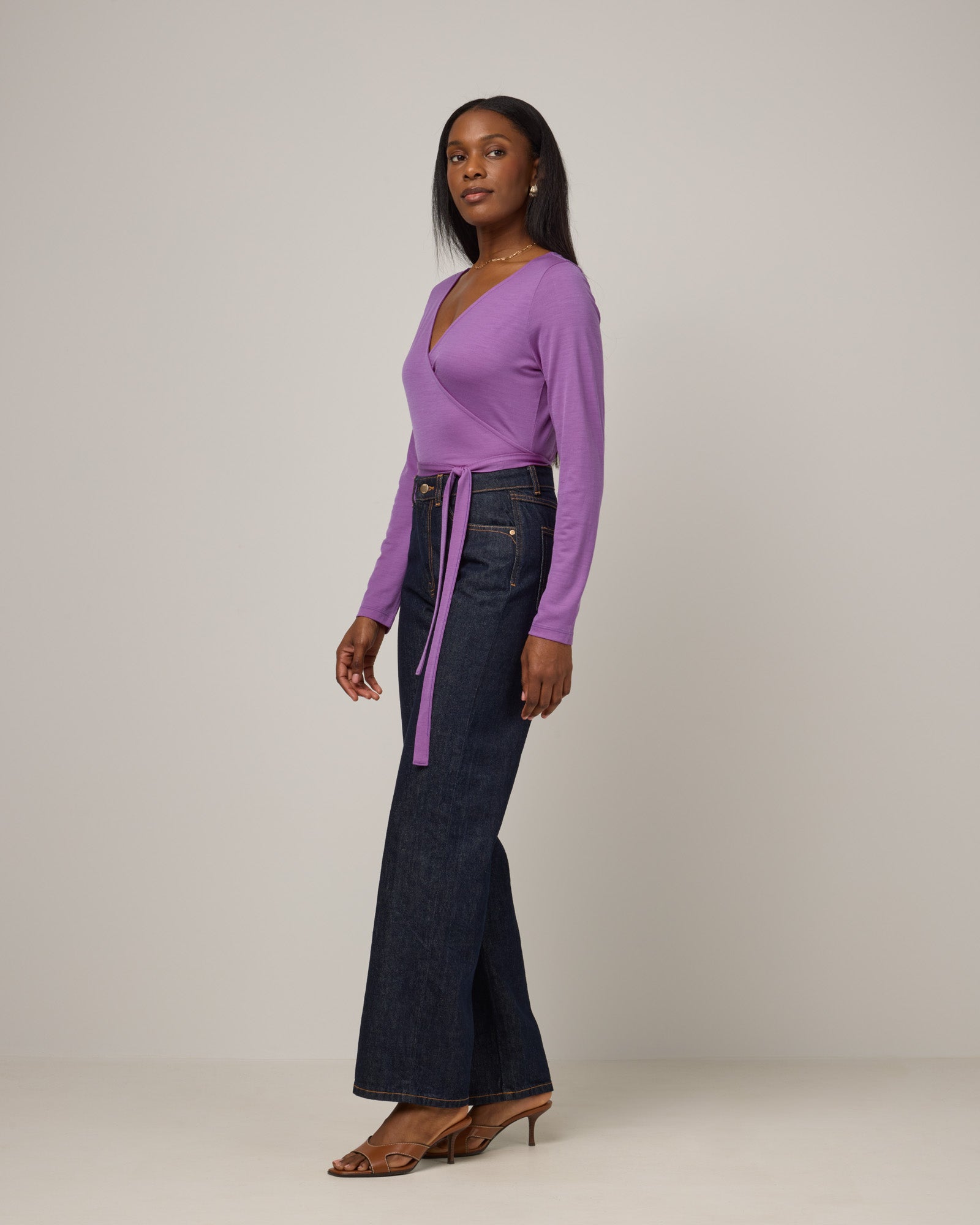 Model wearing Natalia Wrap Top in Purple Pansy, a bright, saturated purple color. Natalia Wrap Top is a merino wool long sleeve, v-neck, slim fit top available in sizes XS-3X.