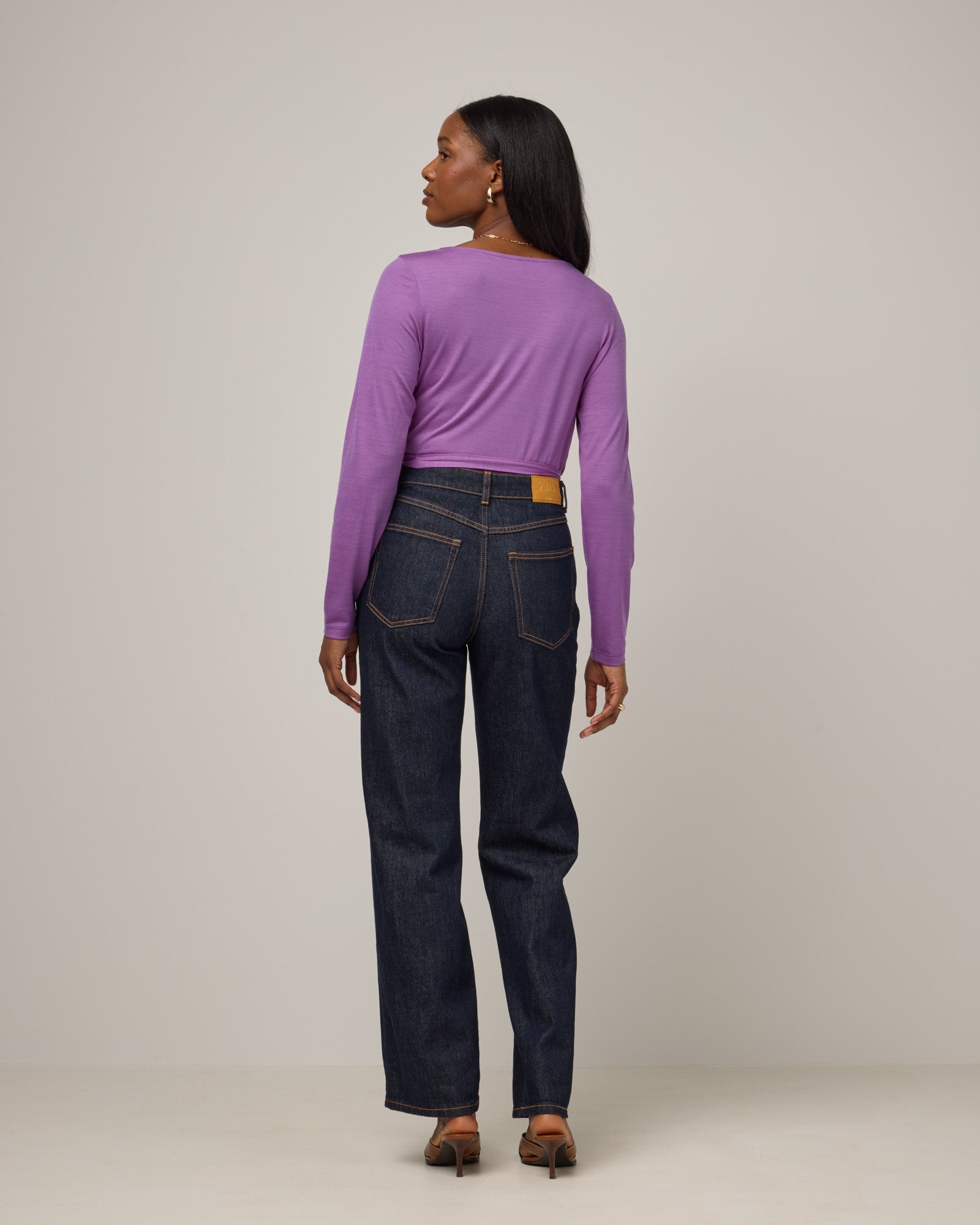 Model wearing Natalia Wrap Top in Purple Pansy, a bright, saturated purple color. Natalia Wrap Top is a merino wool long sleeve, v-neck, slim fit top available in sizes XS-3X.