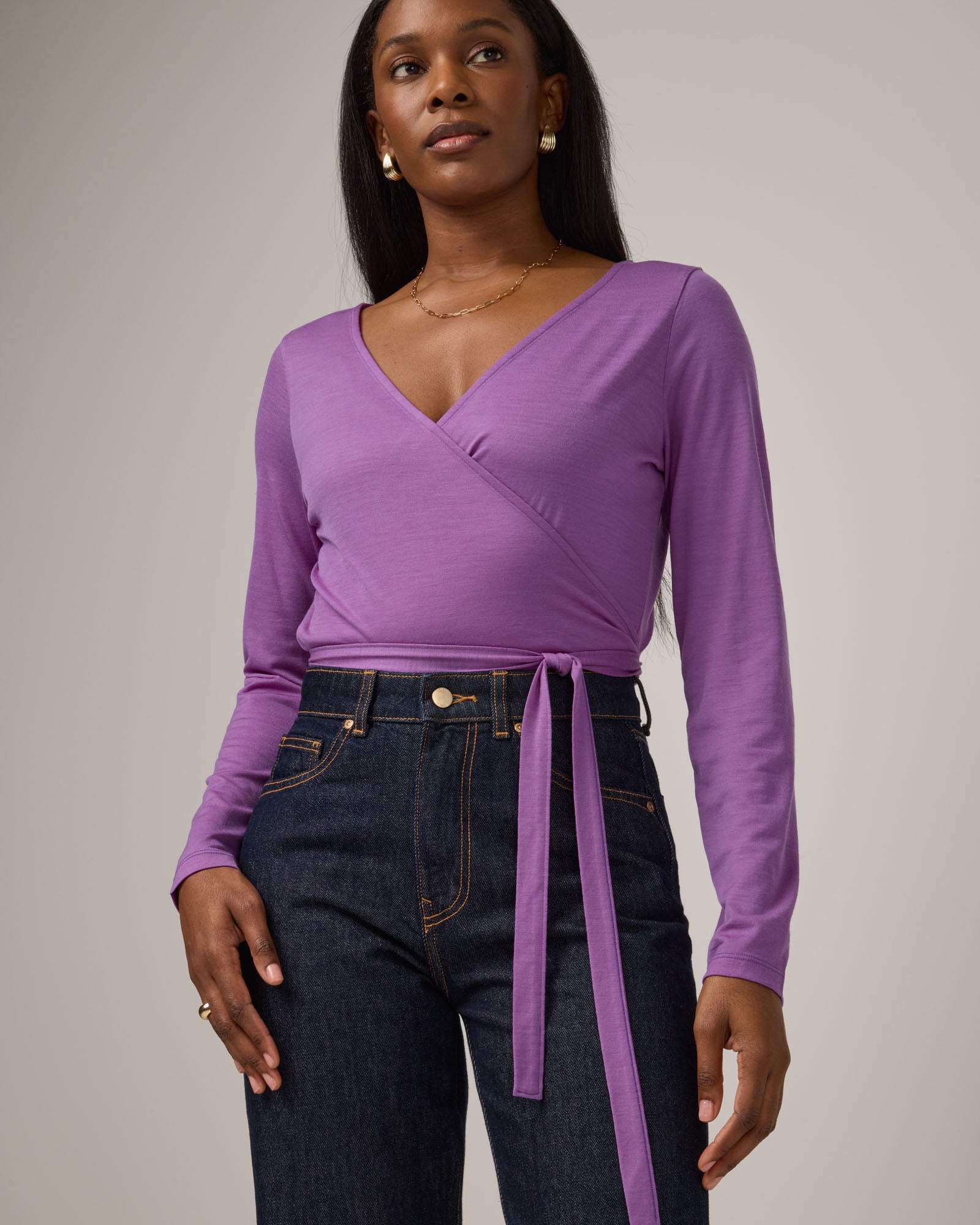 Model wearing Natalia Wrap Top in Purple Pansy, a bright, saturated purple color. Natalia Wrap Top is a merino wool long sleeve, v-neck, slim fit top available in sizes XS-3X.