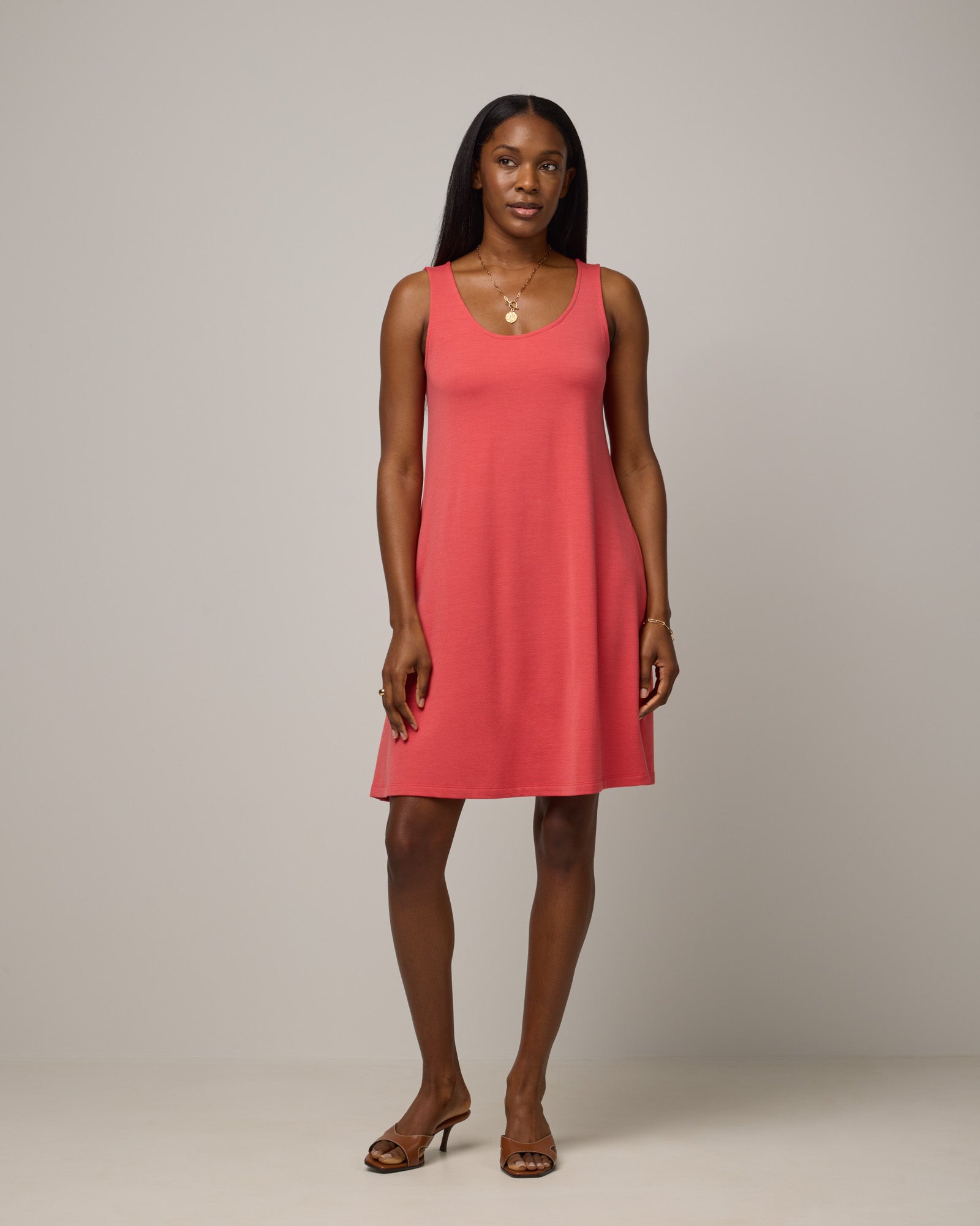 Model wearing Drew Tank Dress in Fruit Punch, a vivid red-orange color. Drew Tank Dress is a merino wool sleeveless, scoop neck, knee length swing dress available in sizes XS-3X.