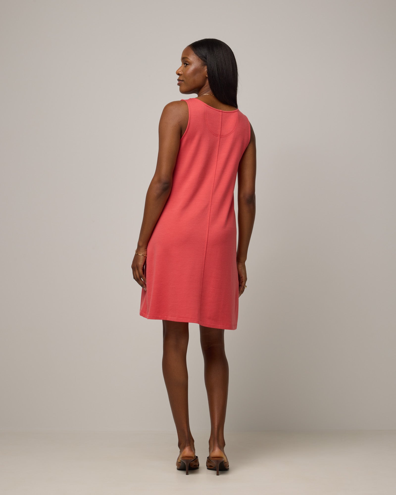 Model wearing Drew Tank Dress in Fruit Punch, a vivid red-orange color. Drew Tank Dress is a merino wool sleeveless, scoop neck, knee length swing dress available in sizes XS-3X.