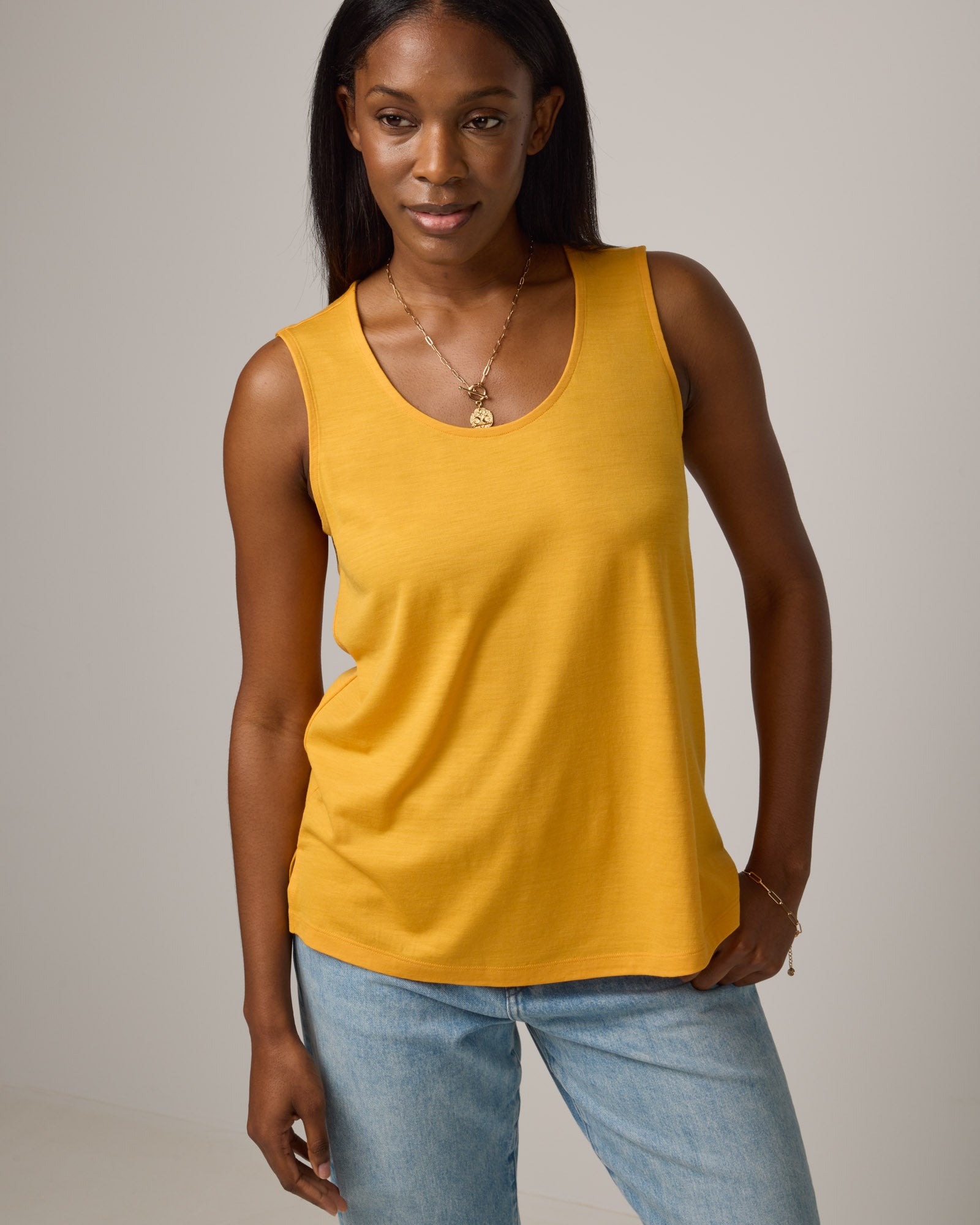 Model wearing Steph Scoop Neck Tank in Mango, a bright yellow-orange color. Steph Scoop Neck Tank is a merino wool sleeveless tank available in sizes XS-3X. 