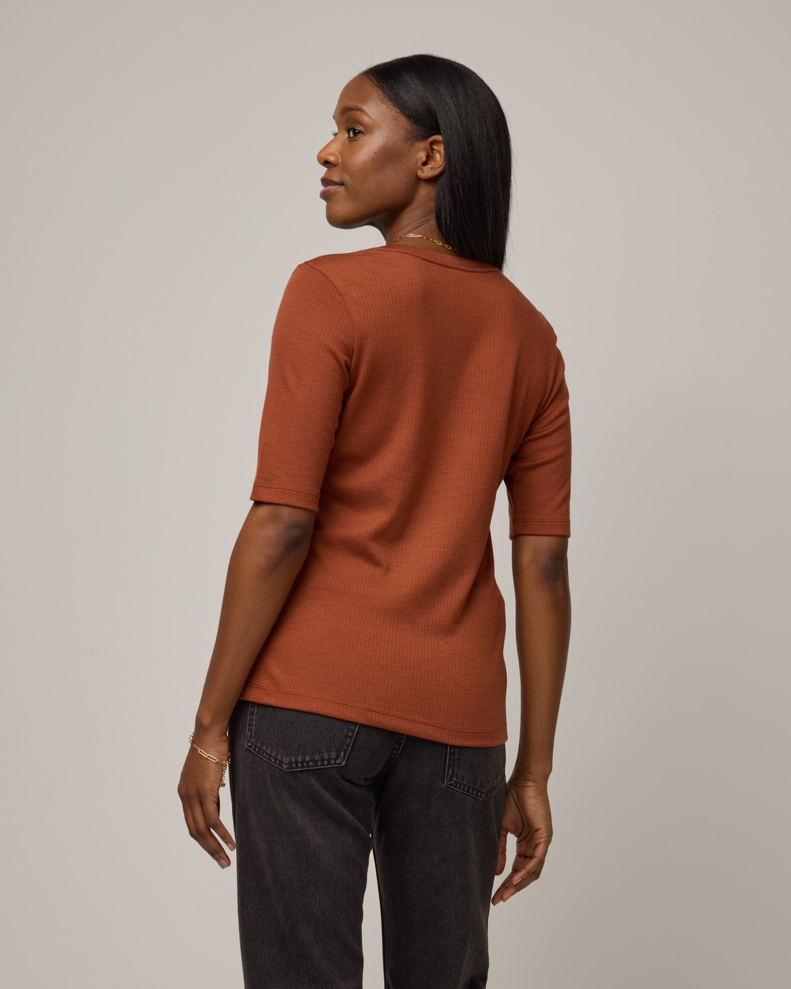 Model wearing Celine Ribbed Elbow Sleeve Tee in Cinnamon, a reddish-brown rust color. Celine Ribbed Elbow Sleeve Tee is a merino wool short sleeve, scoop neck tee available in sizes XS-3X.