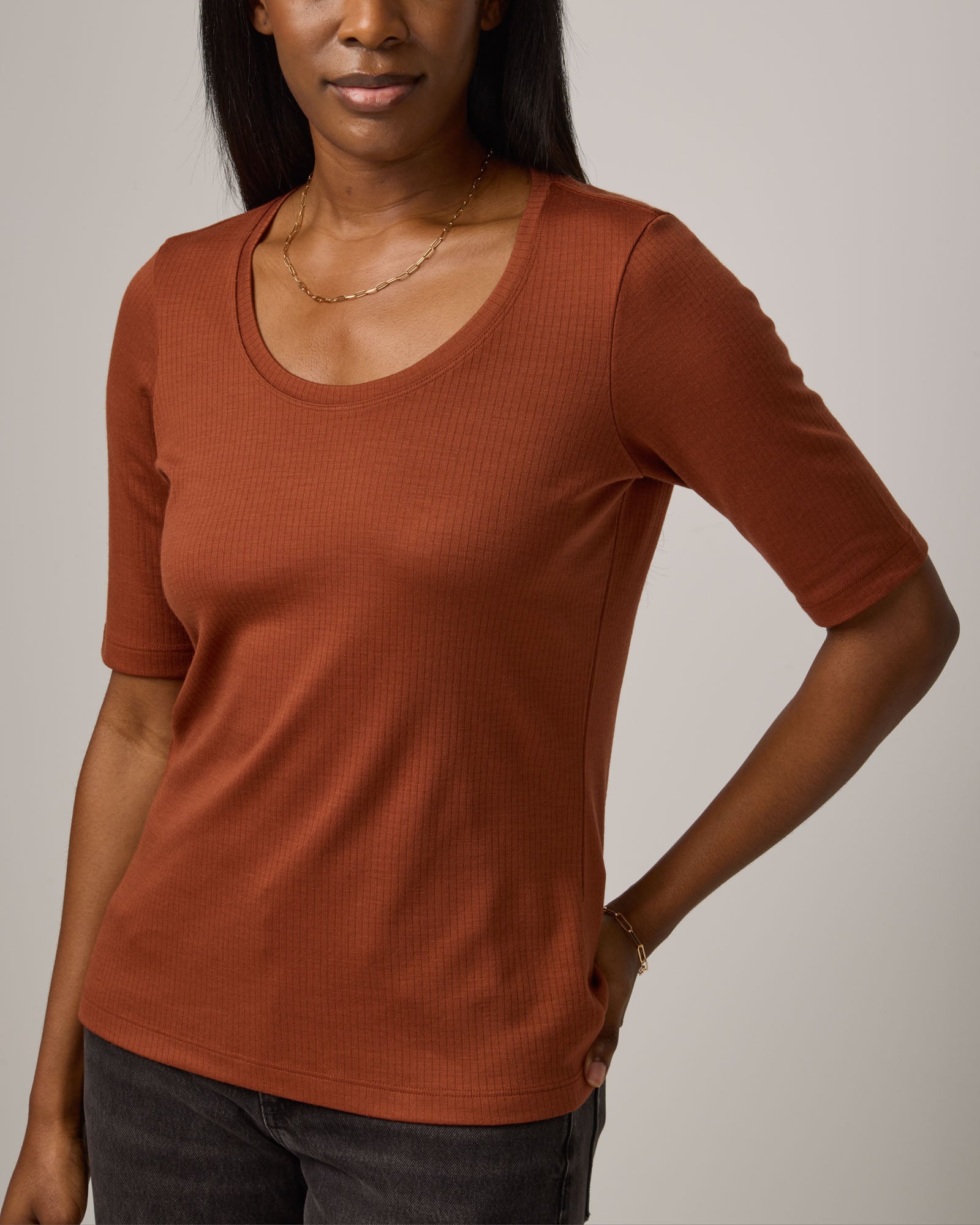 Model wearing Celine Ribbed Elbow Sleeve Tee in Cinnamon, a reddish-brown rust color. Celine Ribbed Elbow Sleeve Tee is a merino wool short sleeve, scoop neck tee available in sizes XS-3X.