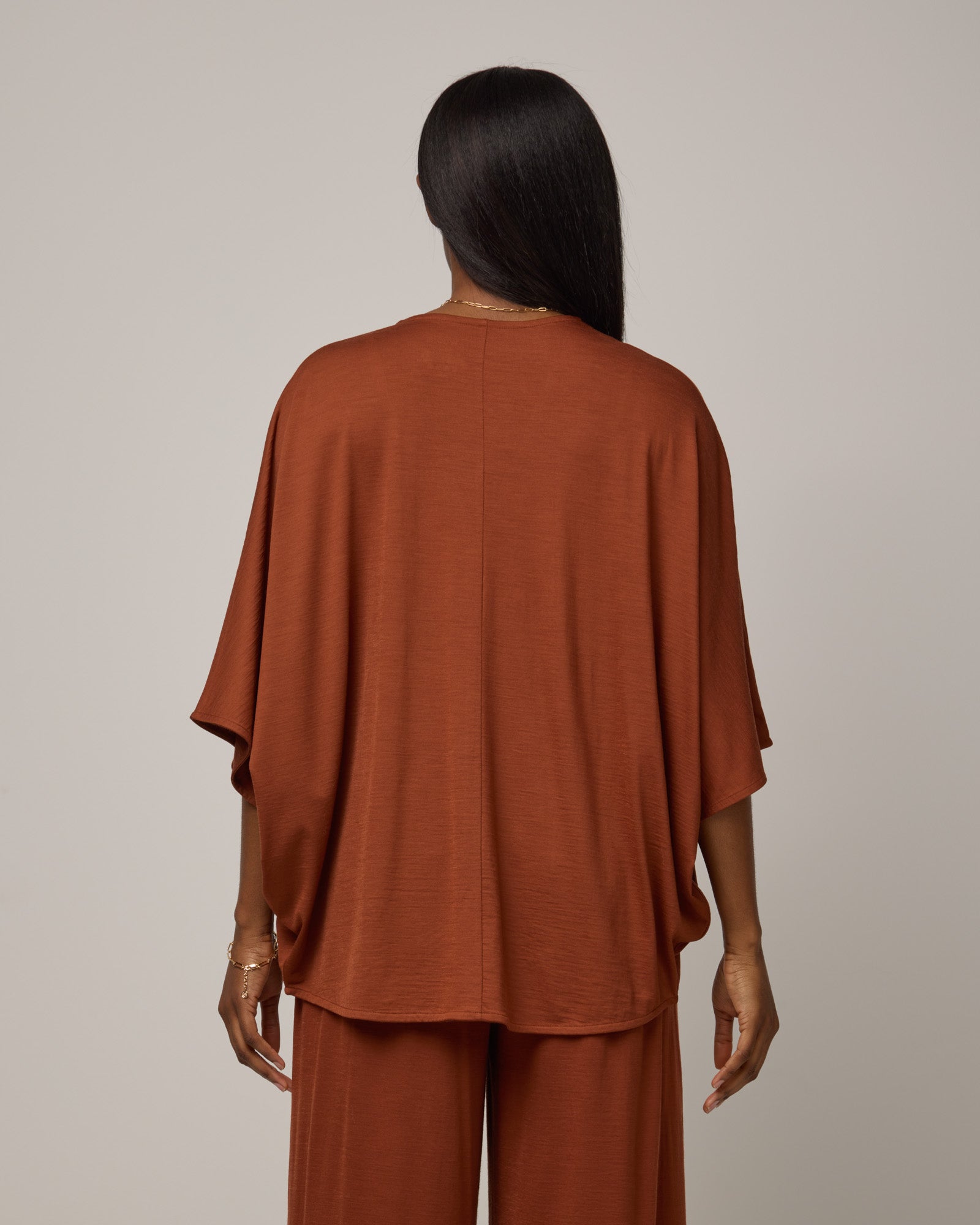 Model wearing Lisbon Shawl Cardigan in Cinnamon, a reddish-brown rust color. Lisbon Shawl Cardigan is a merino wool short sleeve cardigan available in sizes XS/S-2X/3X.