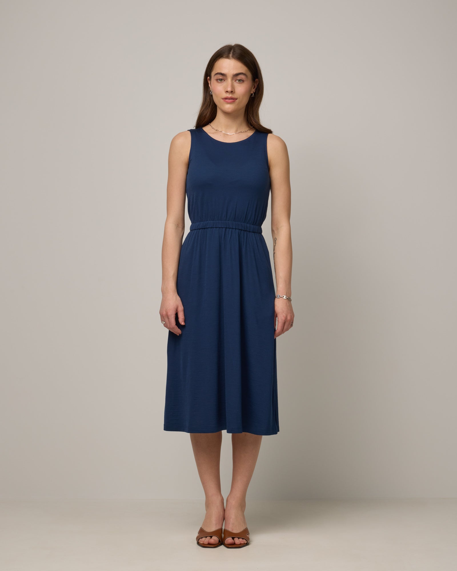 Model wearing Sofia Fit & Flare Dress in Marine Blue, a dark royal blue color. Sofia Fit & Flare Dress is a merino wool sleeveless, crew neck, midi fit & flare dress with pockets available in sizes XS-XXL.