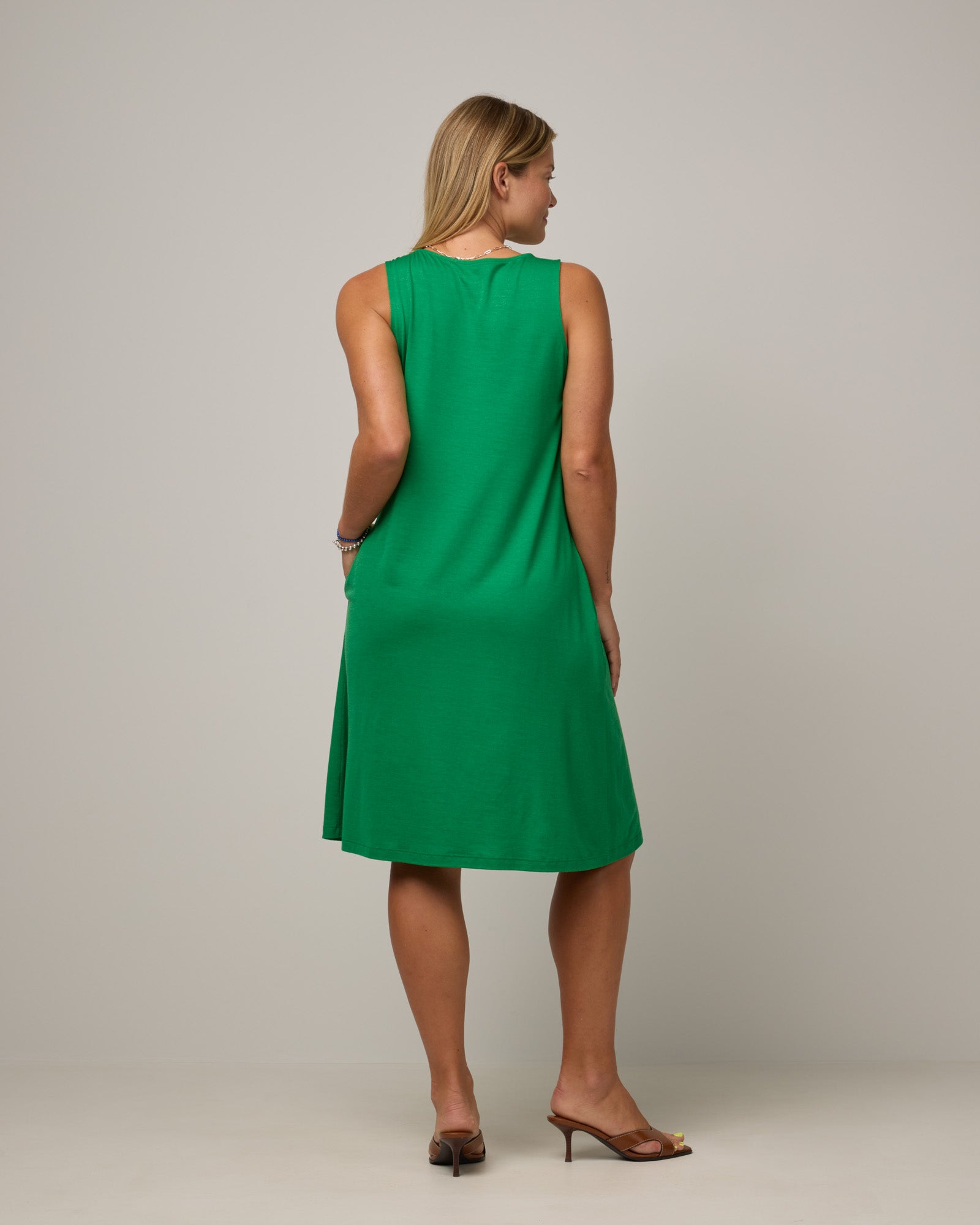 Model wearing Camellia Tank Dress in Verde, a bright Kelly green color. Camellia Tank Dress is a merino wool sleeveless, crew neck, knee length swing dress with pockets available in sizes XS-3X Regular, XS-3X Long.