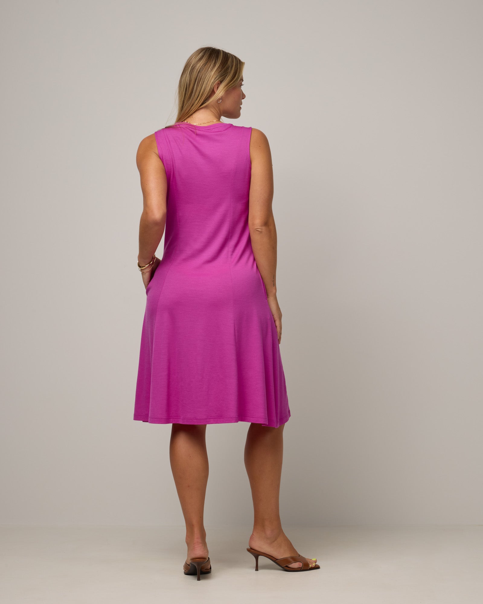 Model wearing Flora Swing Dress in Petunia, a bright fuchsia pink-purple color. Flora Swing Dress is a merino wool sleeveless, scoop neck, knee length swing dress with pockets available in sizes XS-3X.