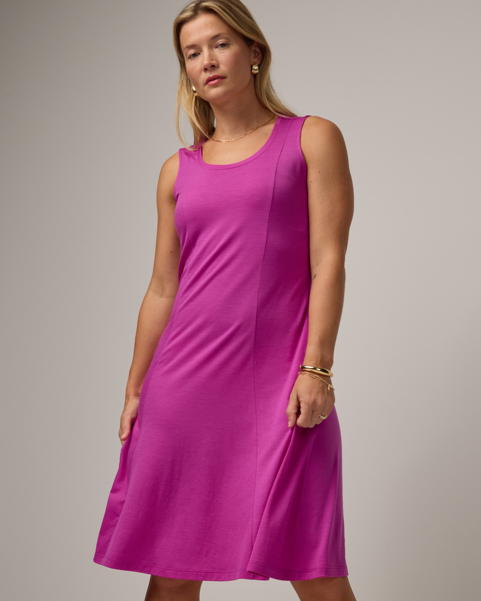 Model wearing Flora Swing Dress in Petunia, a bright fuchsia pink-purple color. Flora Swing Dress is a merino wool sleeveless, scoop neck, knee length swing dress with pockets available in sizes XS-3X.