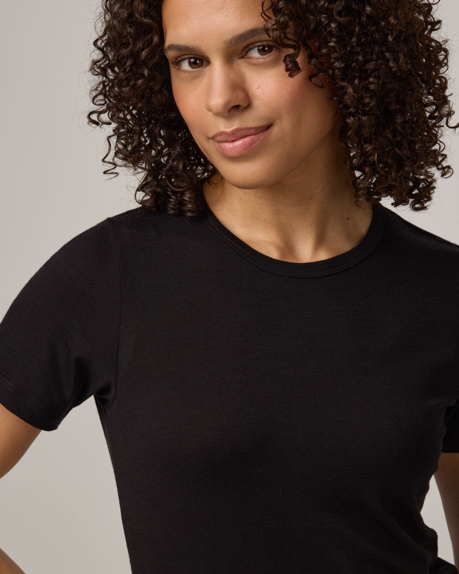 Model wearing Cara 100% Wool Fitted Tee in Black. Cara 100% Wool Fitted Tee is a merino wool short sleeve, crew neck, slim fit tee available in sizes XS-3X.