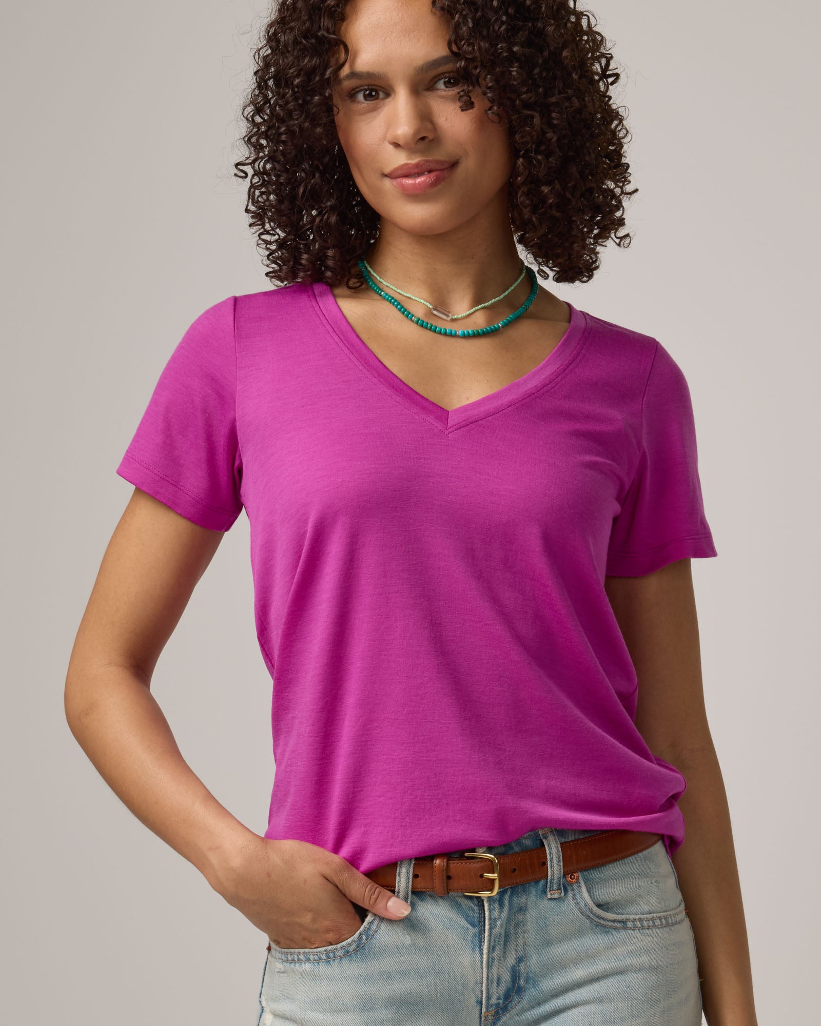 Model wearing Morgan V-Neck Tee in Petunia, a bright berry pink color. Morgan V-Neck Tee is a merino wool short sleeve, v-neck, regular fit tee available in sizes XS-3X.