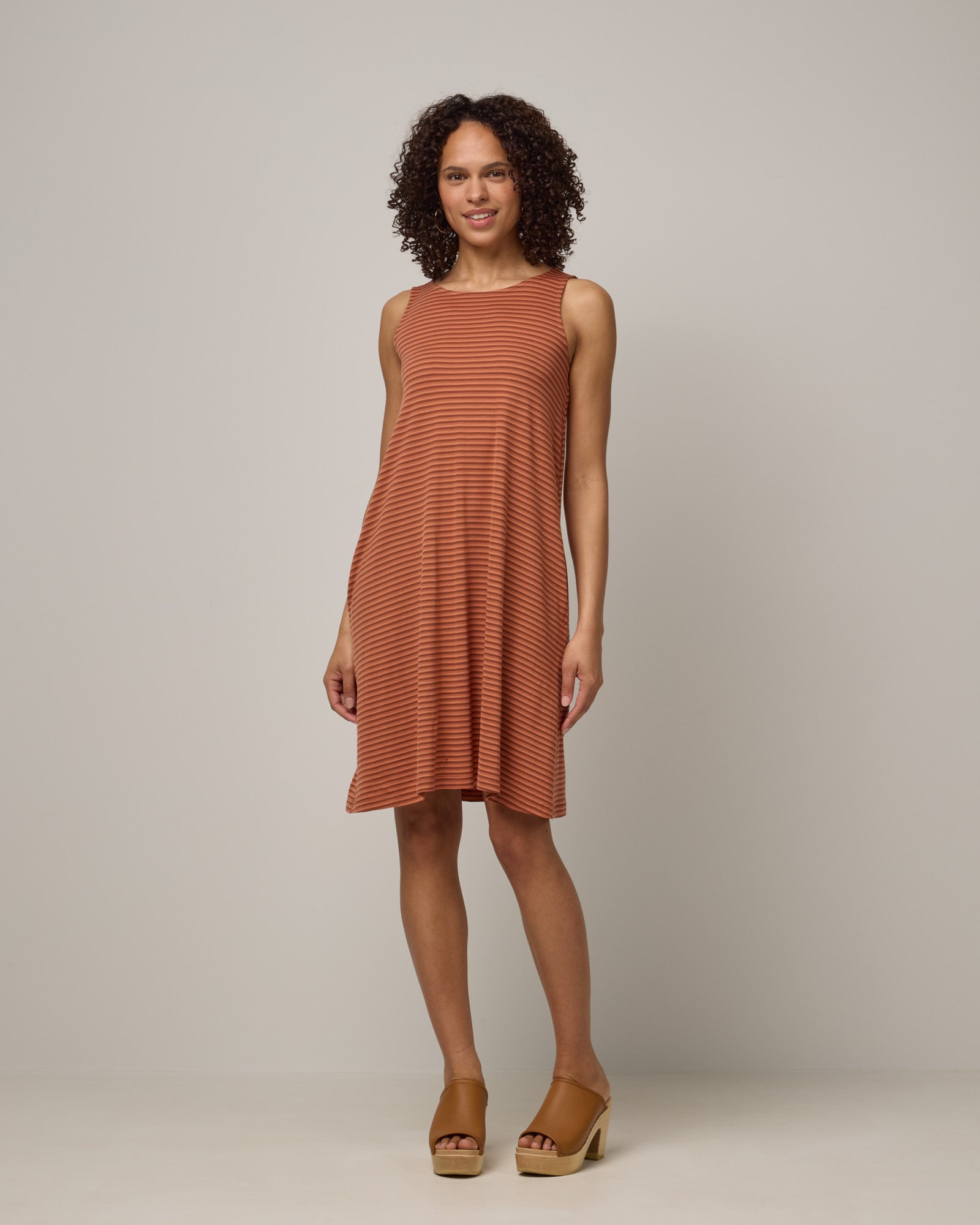 Model wearing Camellia Tank Dress in Cinnamon Tonal Stripe. Camellia Tank Dress is a merino wool sleeveless, crew neck, knee length swing dress with pockets available in sizes XS-3X Regular, XS-3X Long.