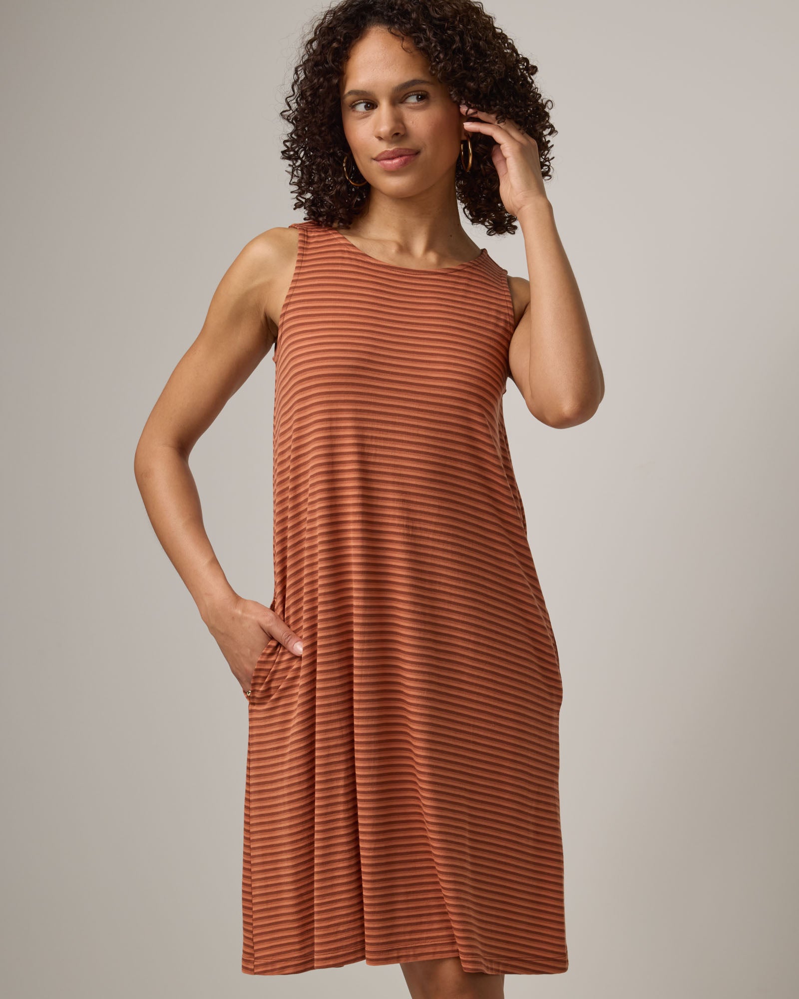 Model wearing Camellia Tank Dress in Cinnamon Tonal Stripe. Camellia Tank Dress is a merino wool sleeveless, crew neck, knee length swing dress with pockets available in sizes XS-3X Regular, XS-3X Long.