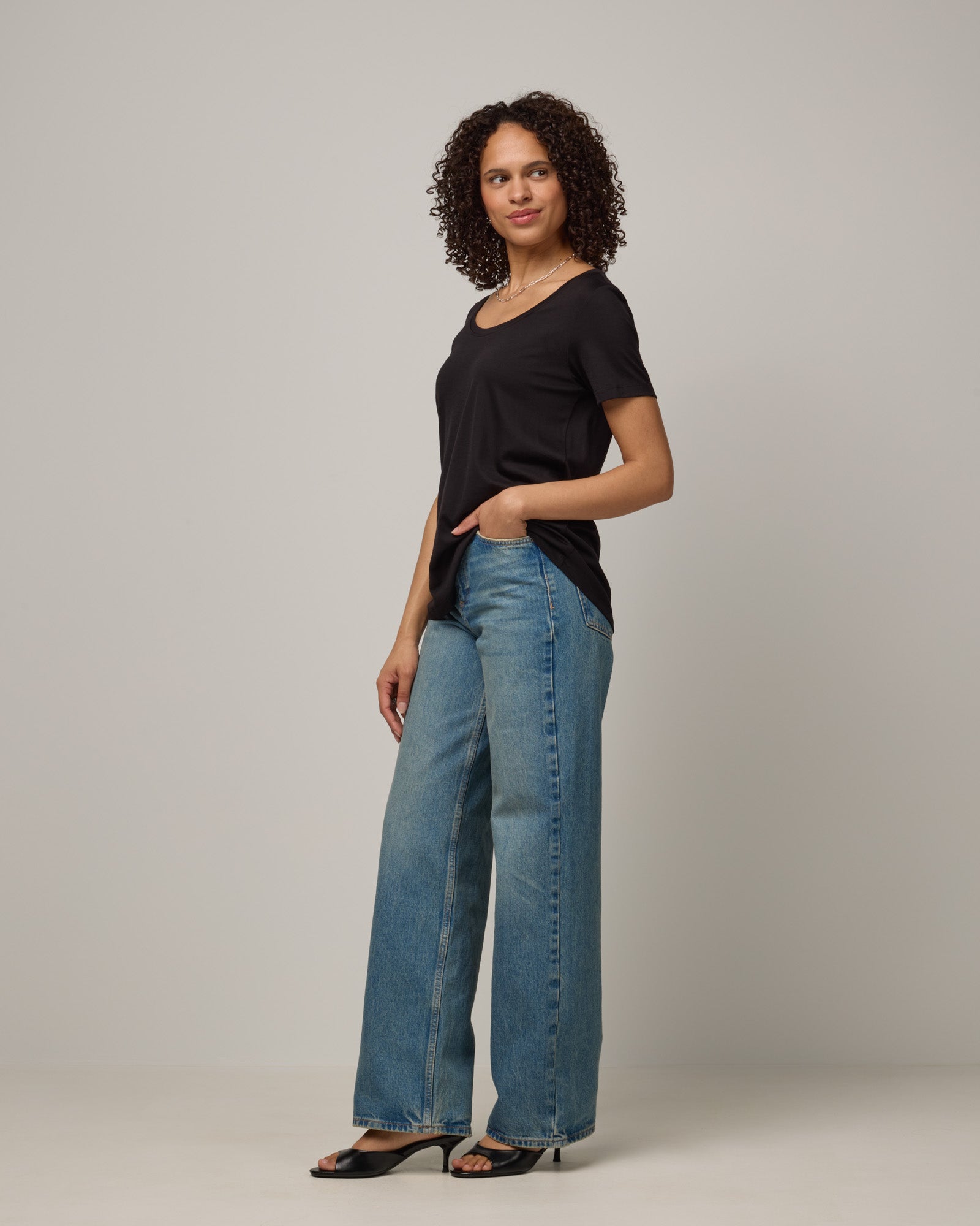 Model wearing Stella Signature Scoop Neck Tee in Black. Stella Signature Scoop Neck Tee is a merino wool short sleeve, scoop neck, relaxed fit tee available in sizes XS-3X.