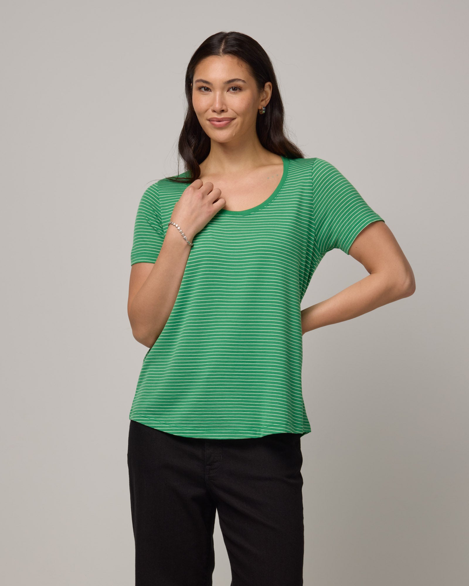 Model wearing Stella Scoop Neck Tee in Verde & Natural White Stripe. Stella Scoop Neck Tee is a merino wool short sleeve, scoop neck t-shirt available in sizes XS-3X.