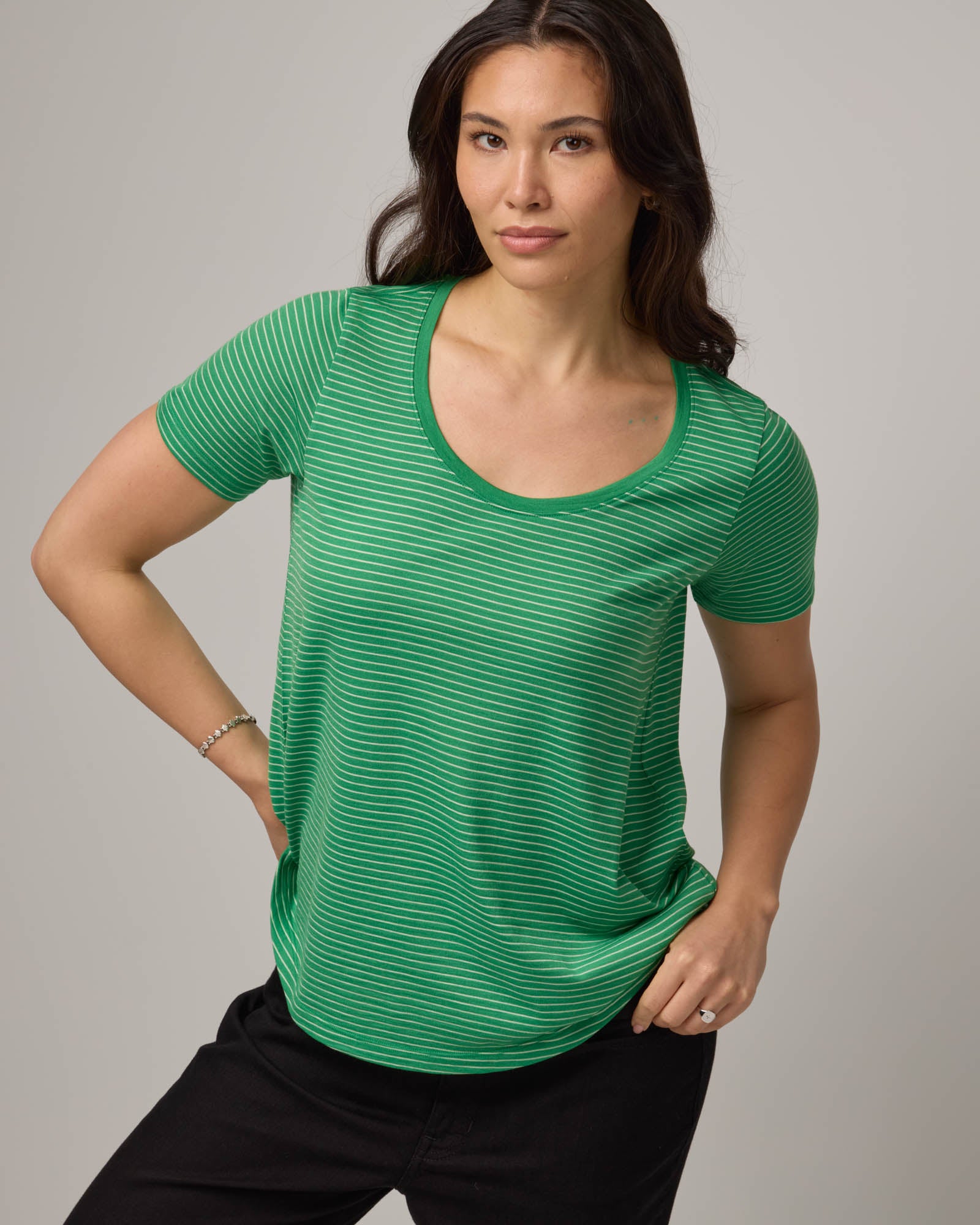 Model wearing Stella Scoop Neck Tee in Verde & Natural White Stripe. Stella Scoop Neck Tee is a merino wool short sleeve, scoop neck t-shirt available in sizes XS-3X.