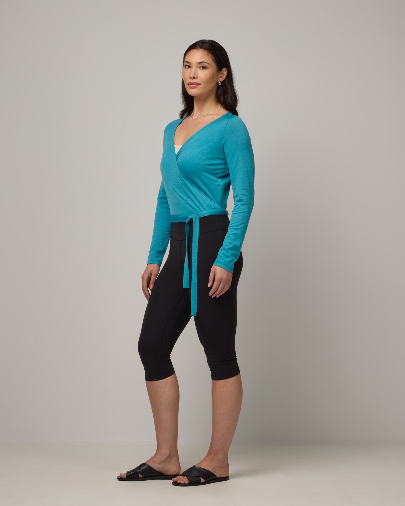 Model wearing Natalia Wrap Top in Sea Blue, a bright sky blue color. Natalia Wrap Top is a merino wool long sleeve, v-neck, slim fit top available in sizes XS-3X.
