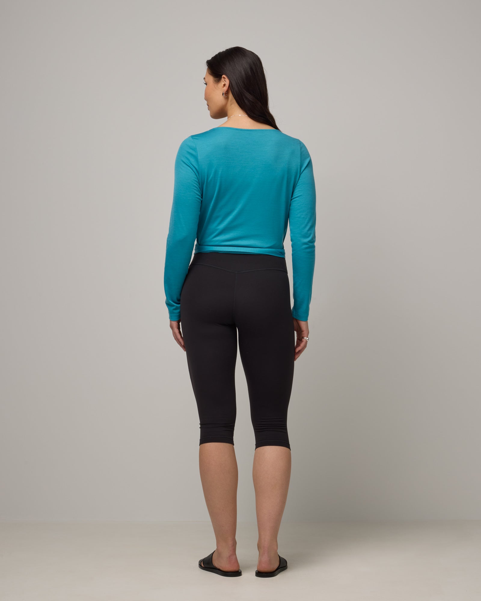 Model wearing Natalia Wrap Top in Sea Blue, a bright sky blue color. Natalia Wrap Top is a merino wool long sleeve, v-neck, slim fit top available in sizes XS-3X.