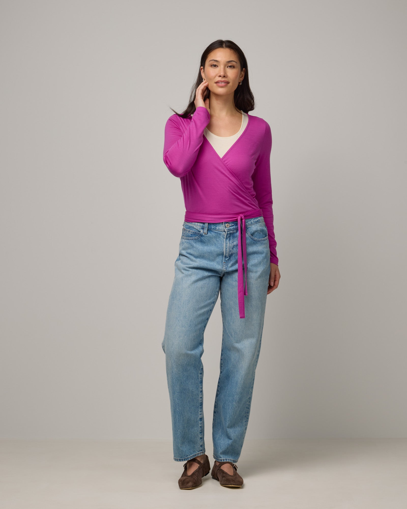 Model wearing Natalia Wrap Top in Petunia, a bright fuchsia pink-purple color. Natalia Wrap Top is a merino wool long sleeve, v-neck, slim fit top available in sizes XS-3X.