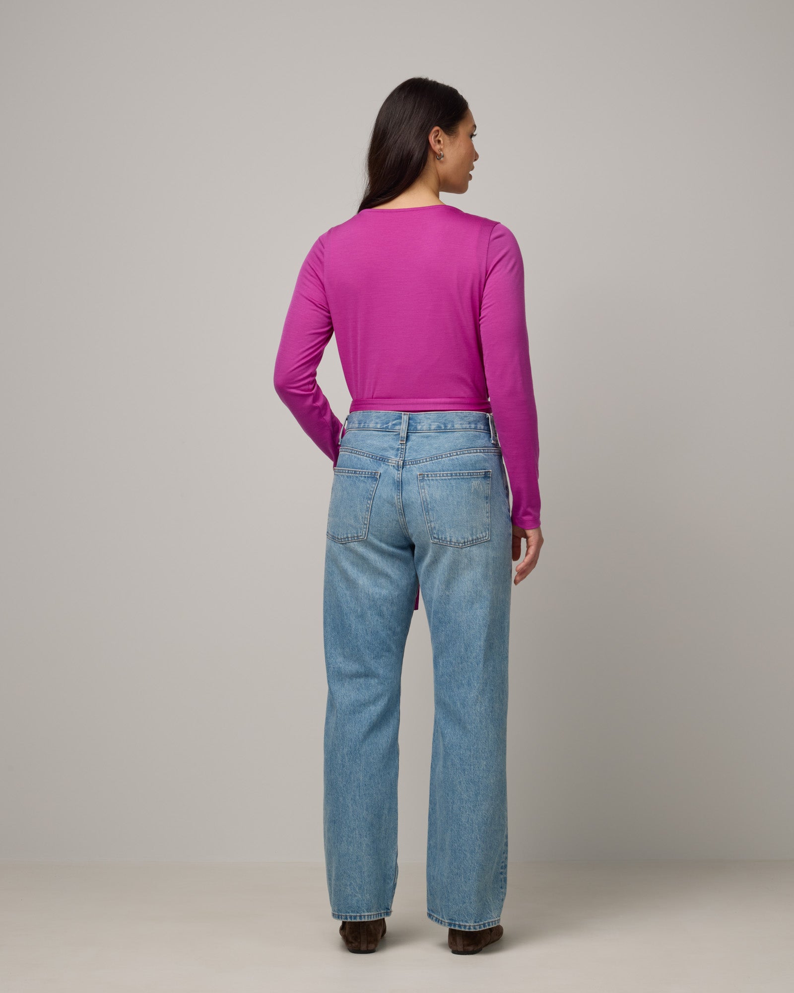 Model wearing Natalia Wrap Top in Petunia, a bright fuchsia pink-purple color. Natalia Wrap Top is a merino wool long sleeve, v-neck, slim fit top available in sizes XS-3X.
