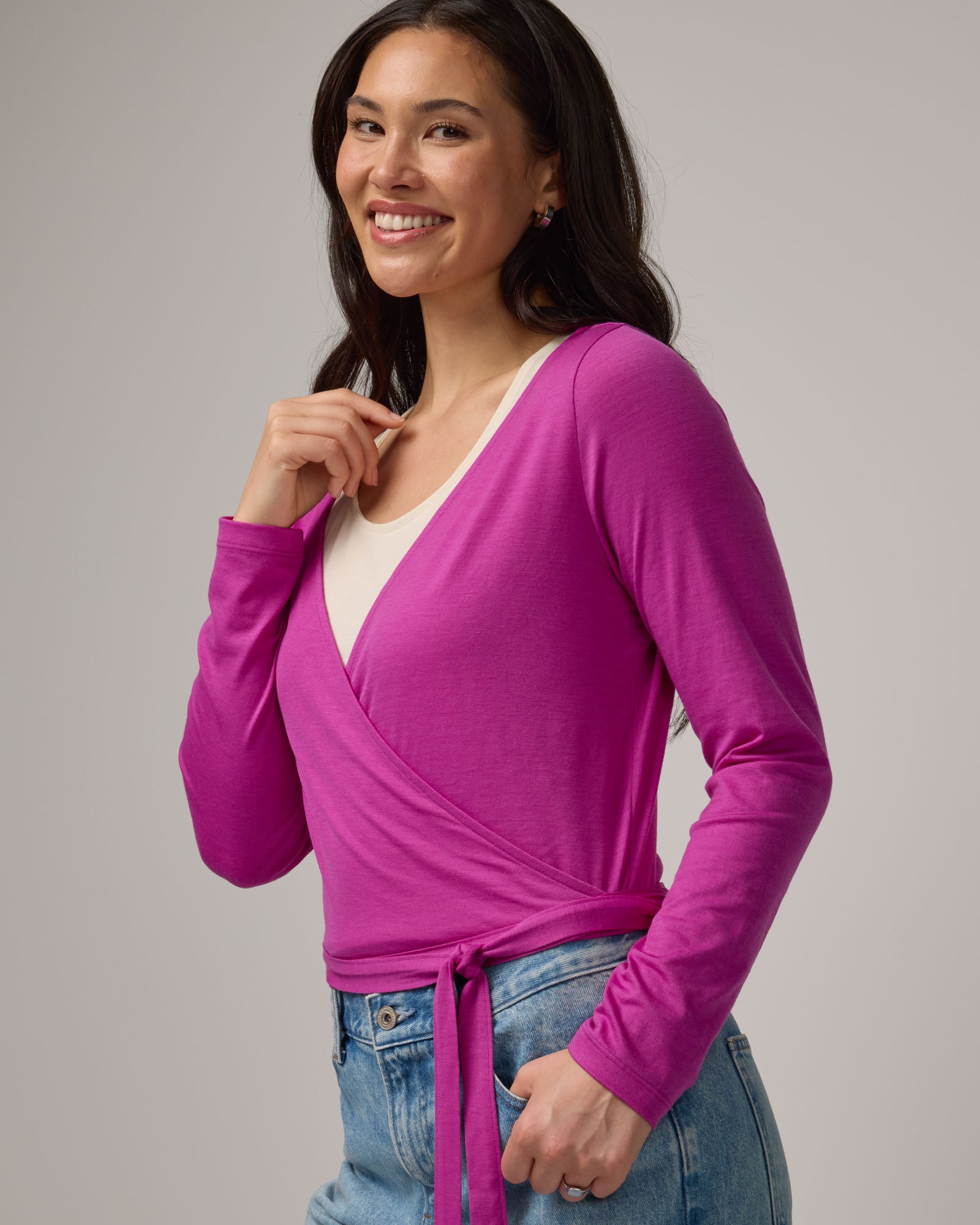 Model wearing Natalia Wrap Top in Petunia, a bright fuchsia pink-purple color. Natalia Wrap Top is a merino wool long sleeve, v-neck, slim fit top available in sizes XS-3X.