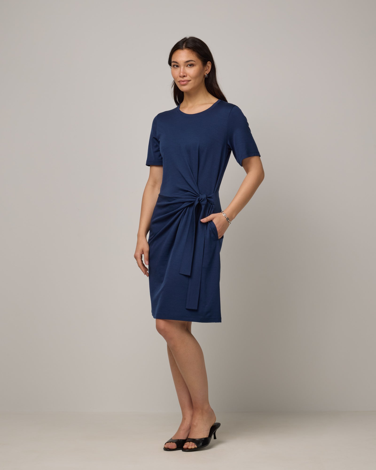 Model wearing Kelly Faux Tie Dress in Marine Blue, a deep royal blue color. Kelly Faux Tie Dress is a merino wool crew neck, short sleeve, knee length shift dress with pockets available in sizes XS-3X. 